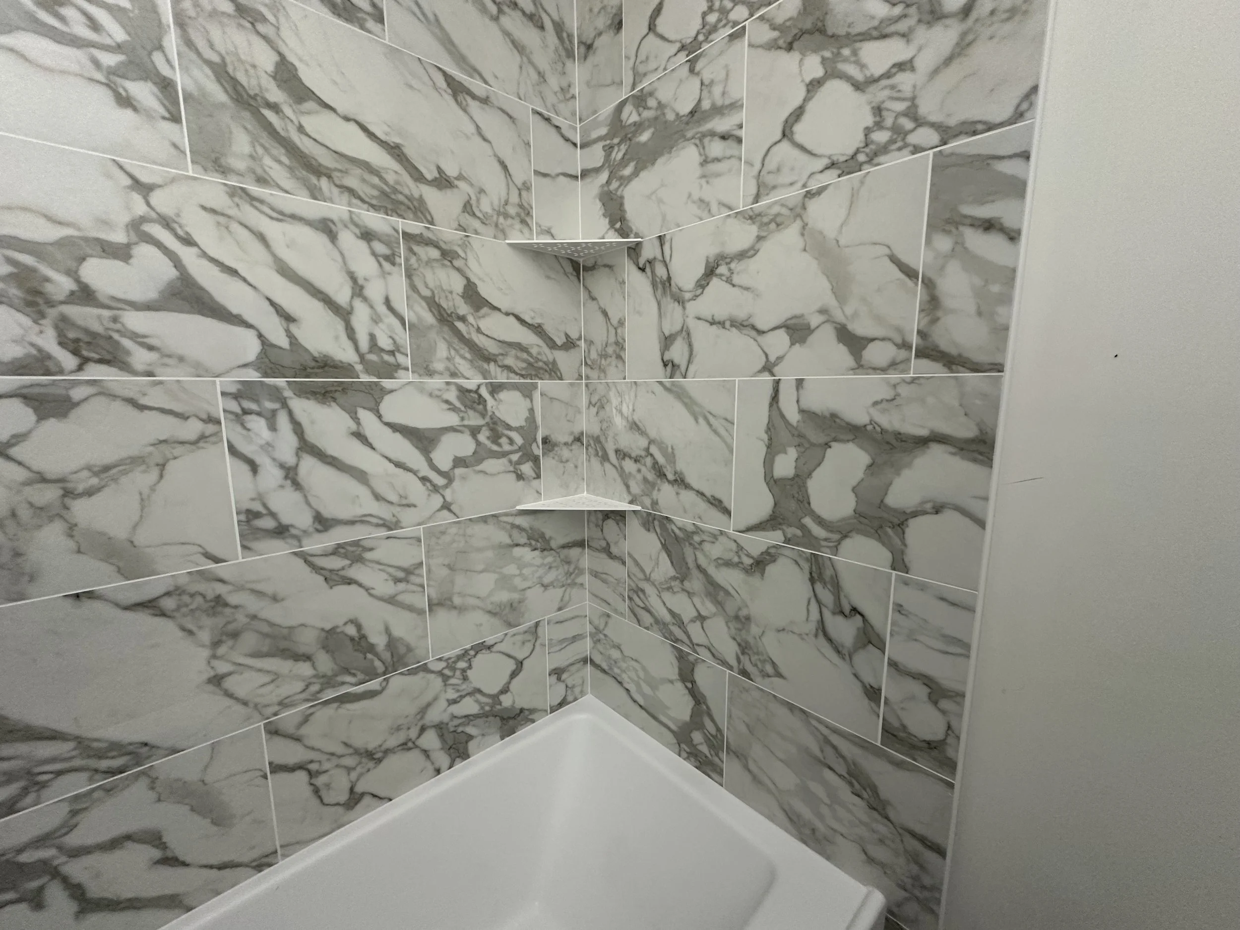 Marble tile wall in a shower with white bathtub at the bottom.
