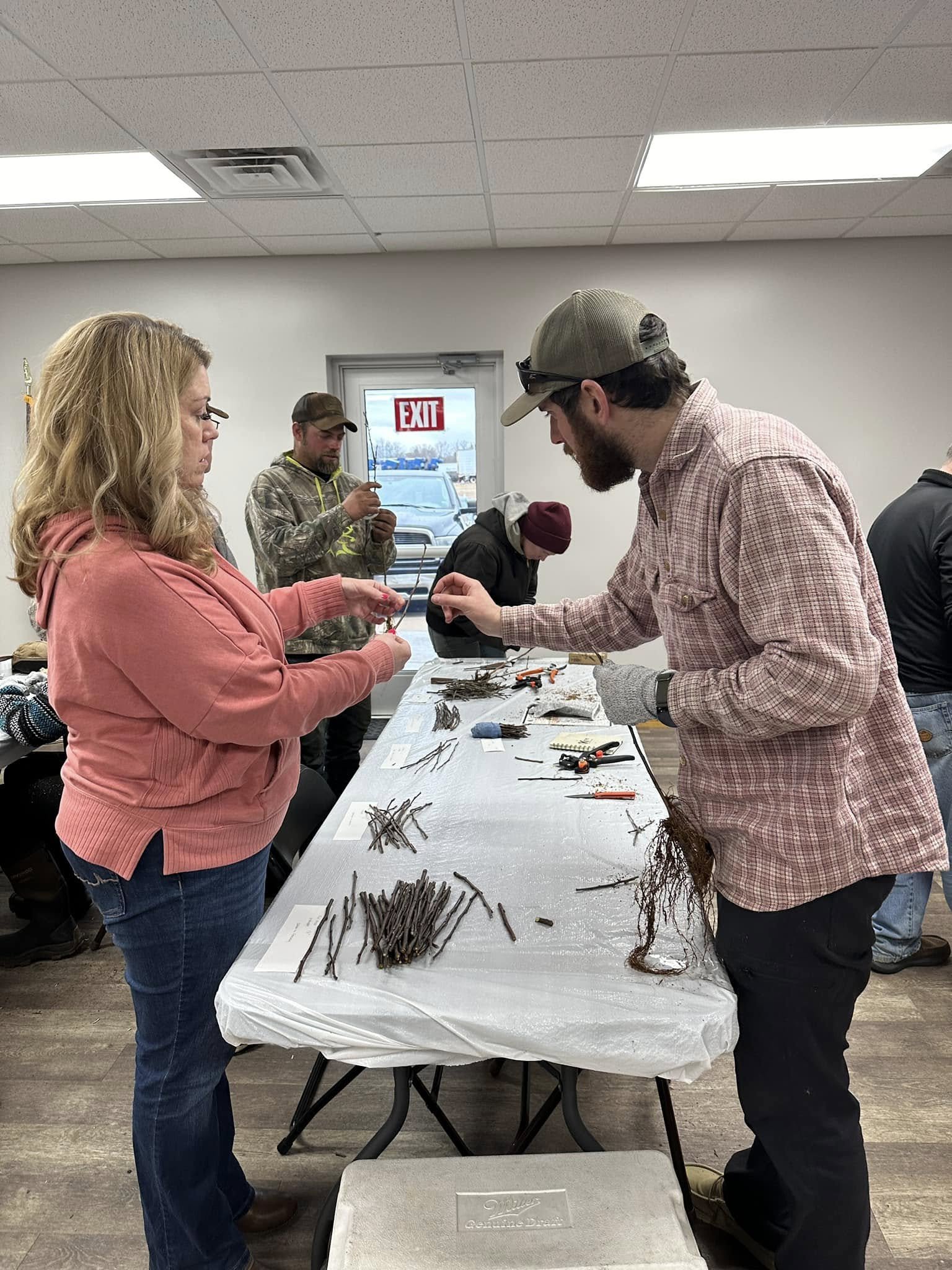 People participating in a fruit tree grafting workshop, handling plant cuttings on a table