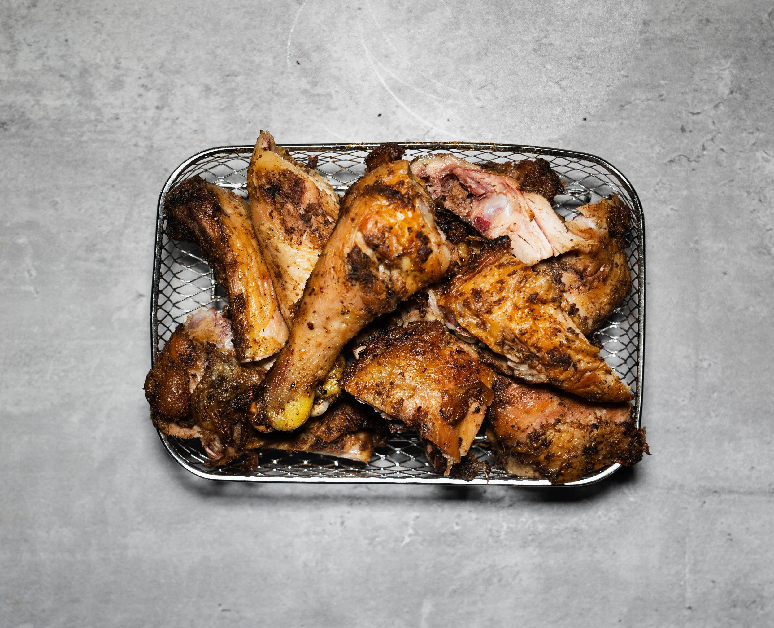 Cooked chicken pieces in a metal wire basket on a grey surface.
