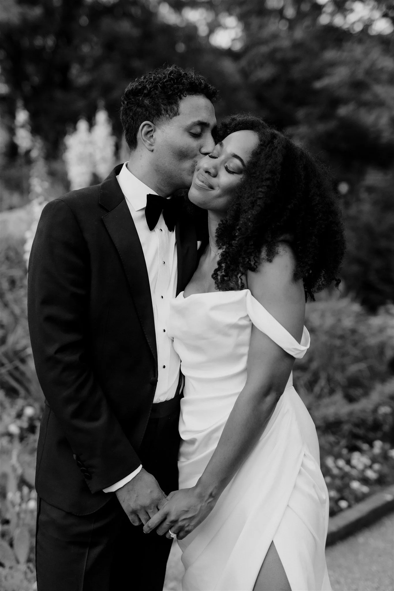 Black and white wedding image of groom kissing bride in destination wedding garden