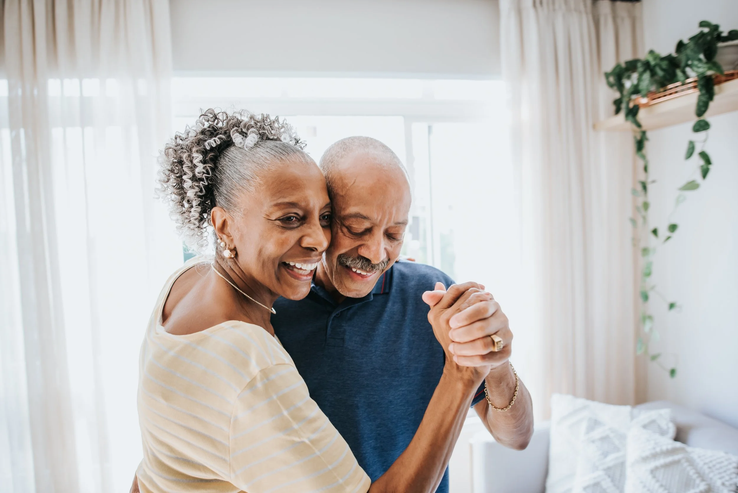 African American couple dancing in a new apartment with white interior finishings and green plants nearby.