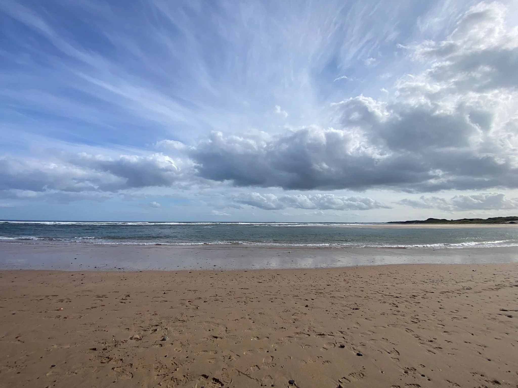 Empty sandy beach with footprints, calm ocean waves, and a cloudy sky.