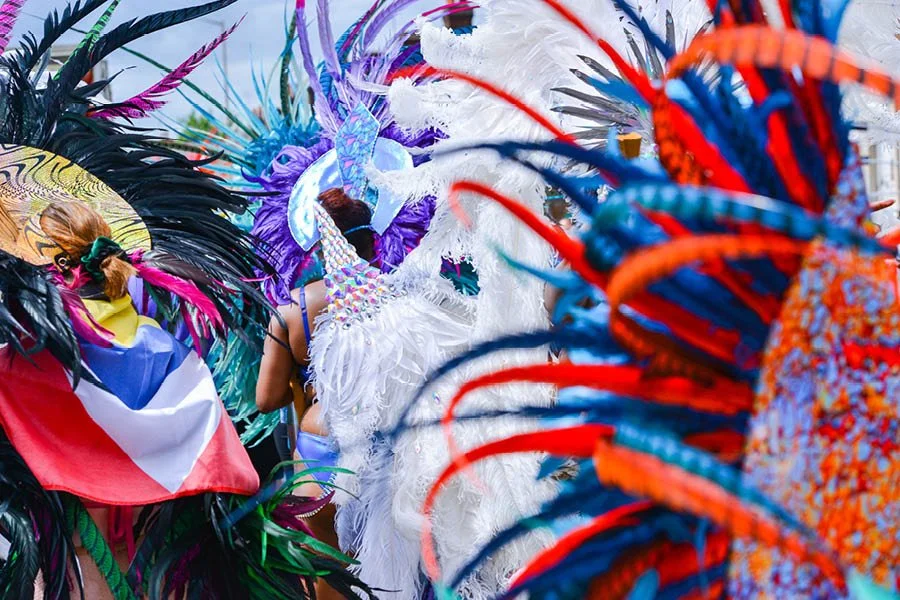 People dressed in colorful Carnival costumes with feathered masks and headdresses at a parade or festival.