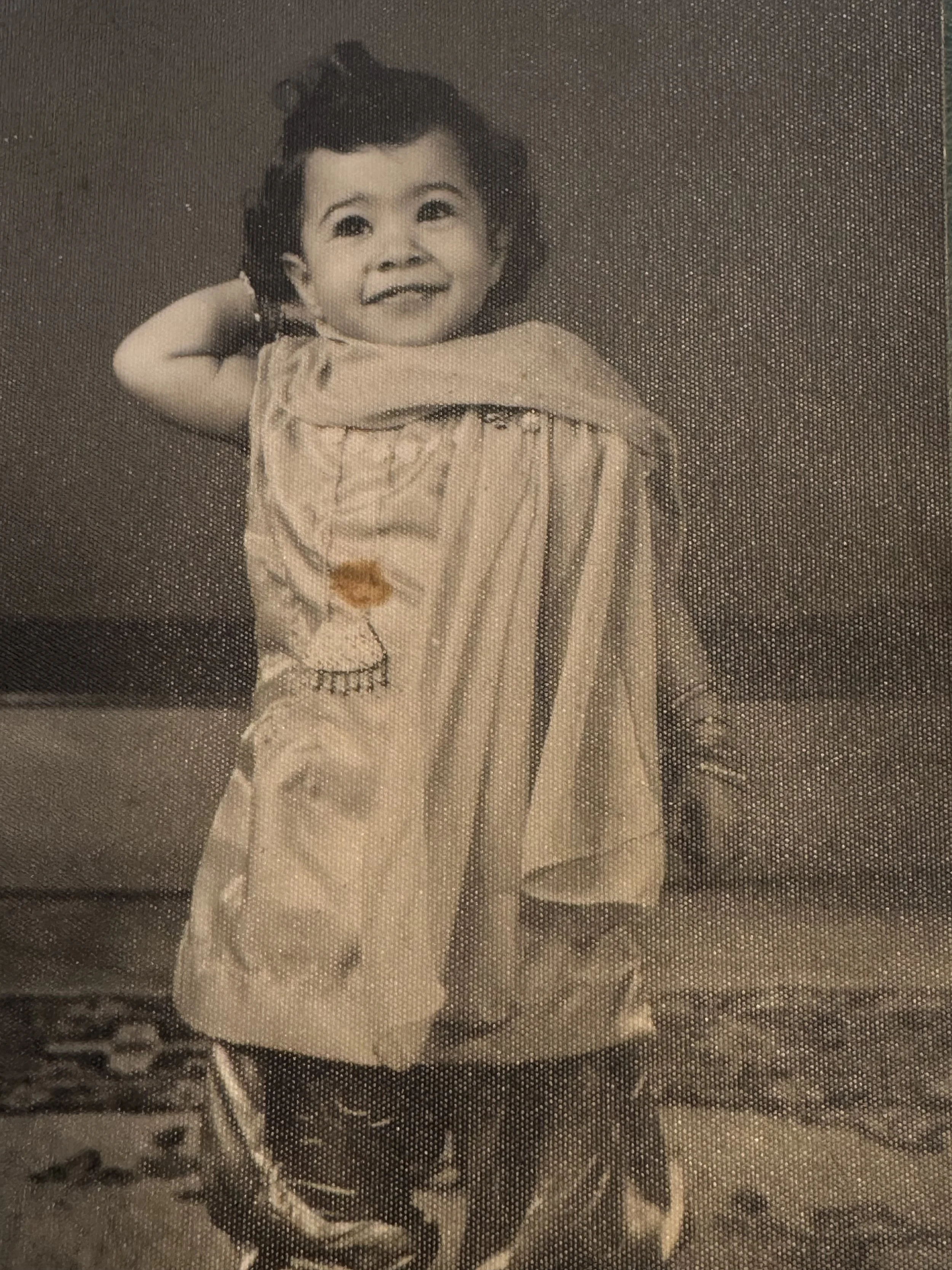 A young Veenaa Saynana Dolphin Heart Alchemy smiling, standing with one arm behind her head. She is wearing a short-sleeve shirt and loose pants, and is standing on a patterned carpet.
