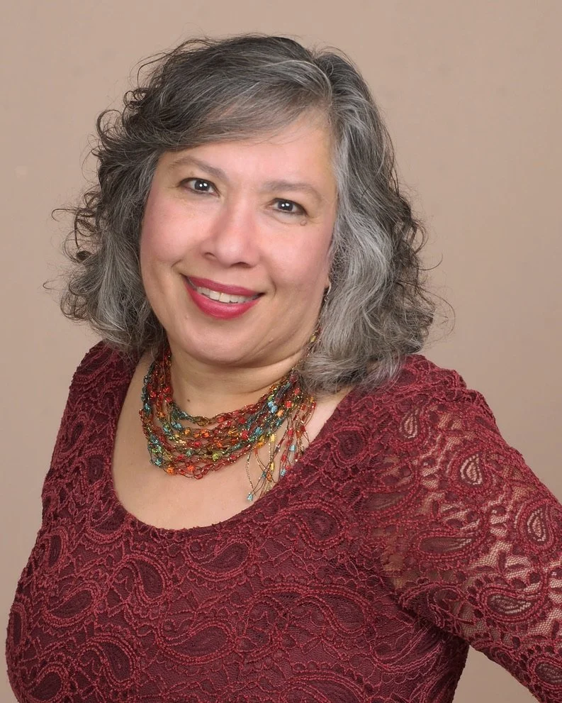 Veenaa Saynana Dolphin Heart Alchemy wearing a maroon lace top and a multicolored beaded necklace, posing in front of a plain beige background.