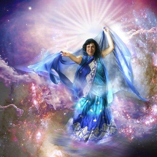 Veenaa Saynana Dolphin Heart Alchemy dressed in a blue and silver costume, standing in front of a cosmic background with stars and nebulae, with light radiating behind them.