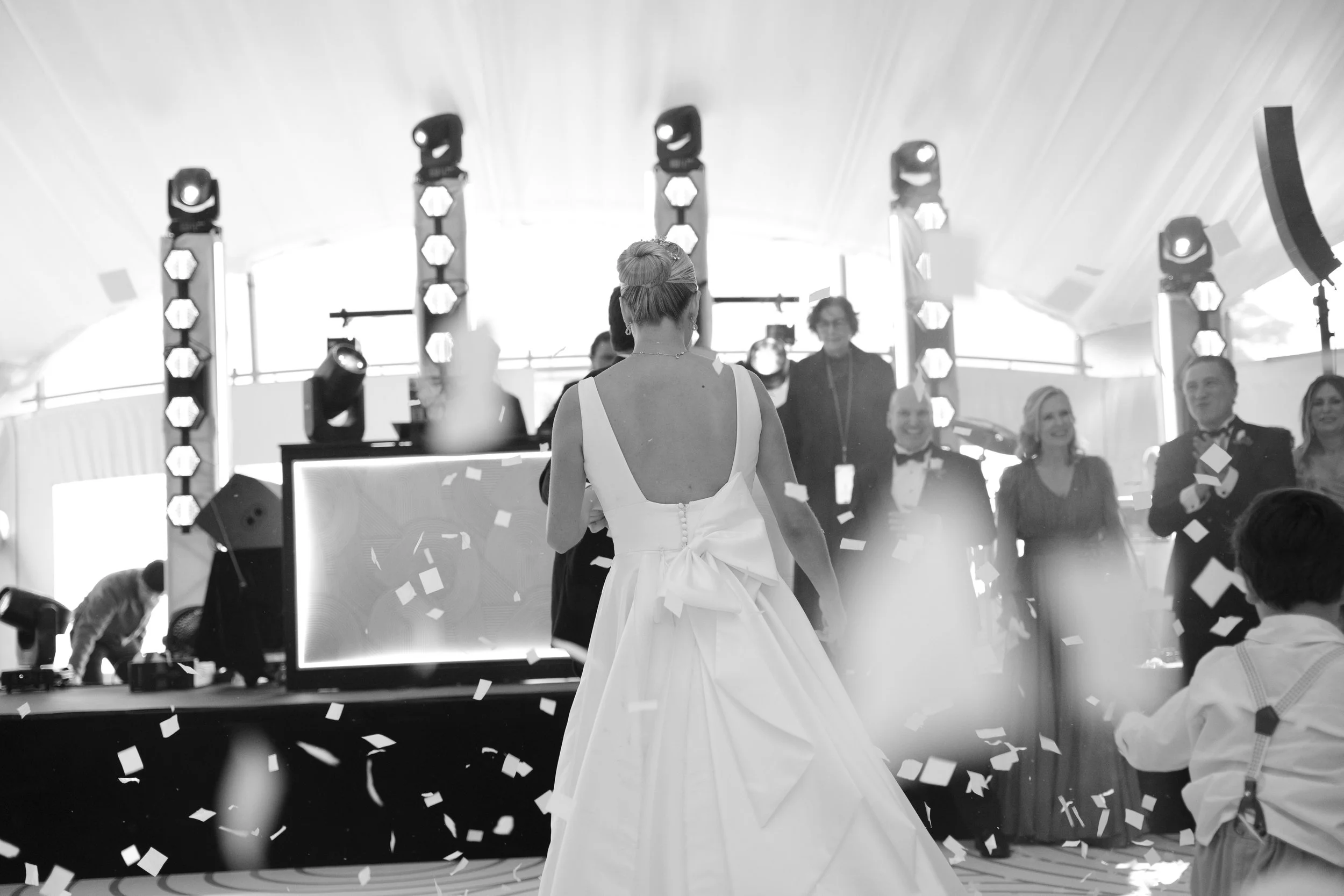 Novia bailando en una celebración con invitados y confeti en un lugar decorado con luces.