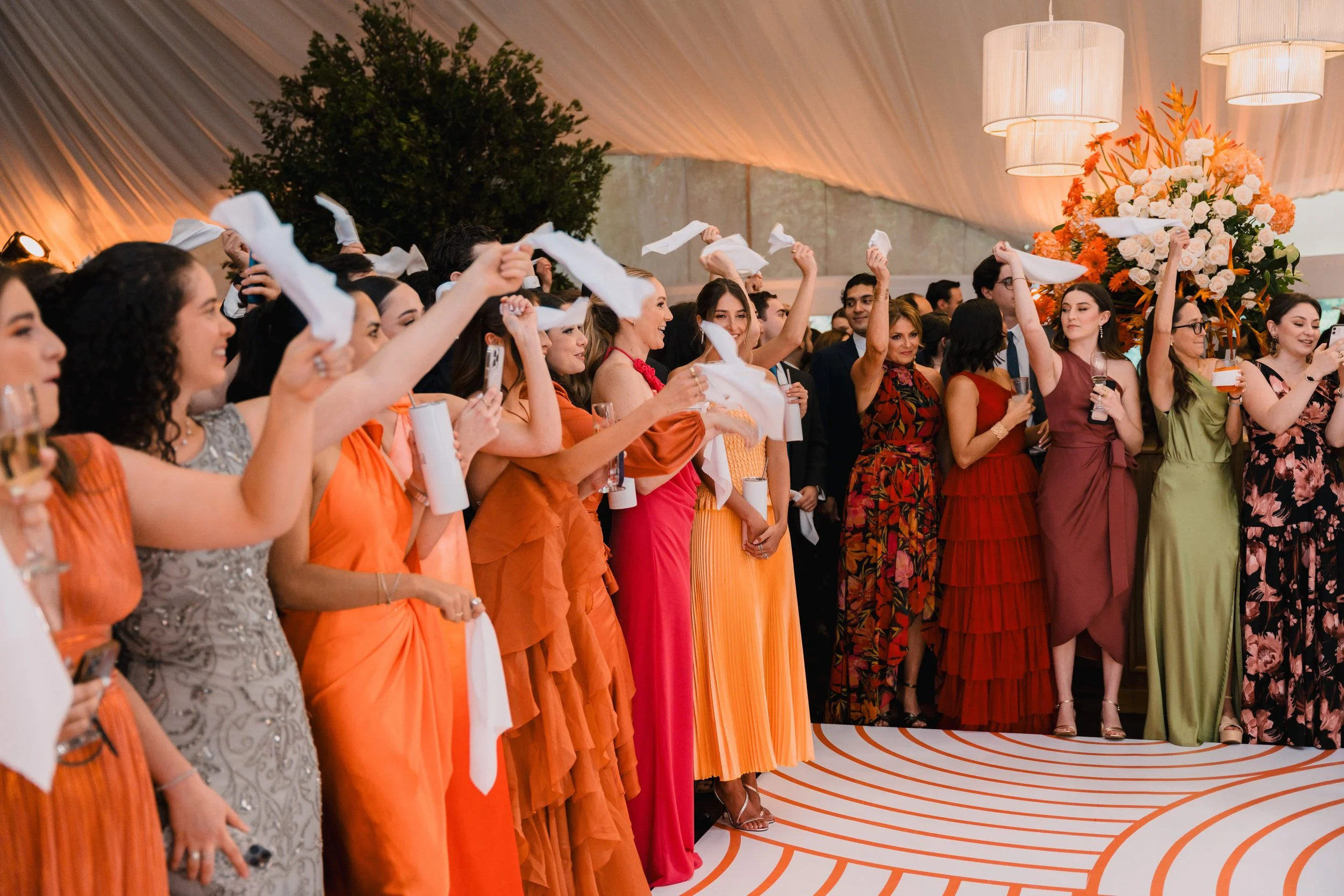 Grupo de personas en un evento, lanzando servilletas al aire en una celebración formal con decoración elegante y flores en el fondo.