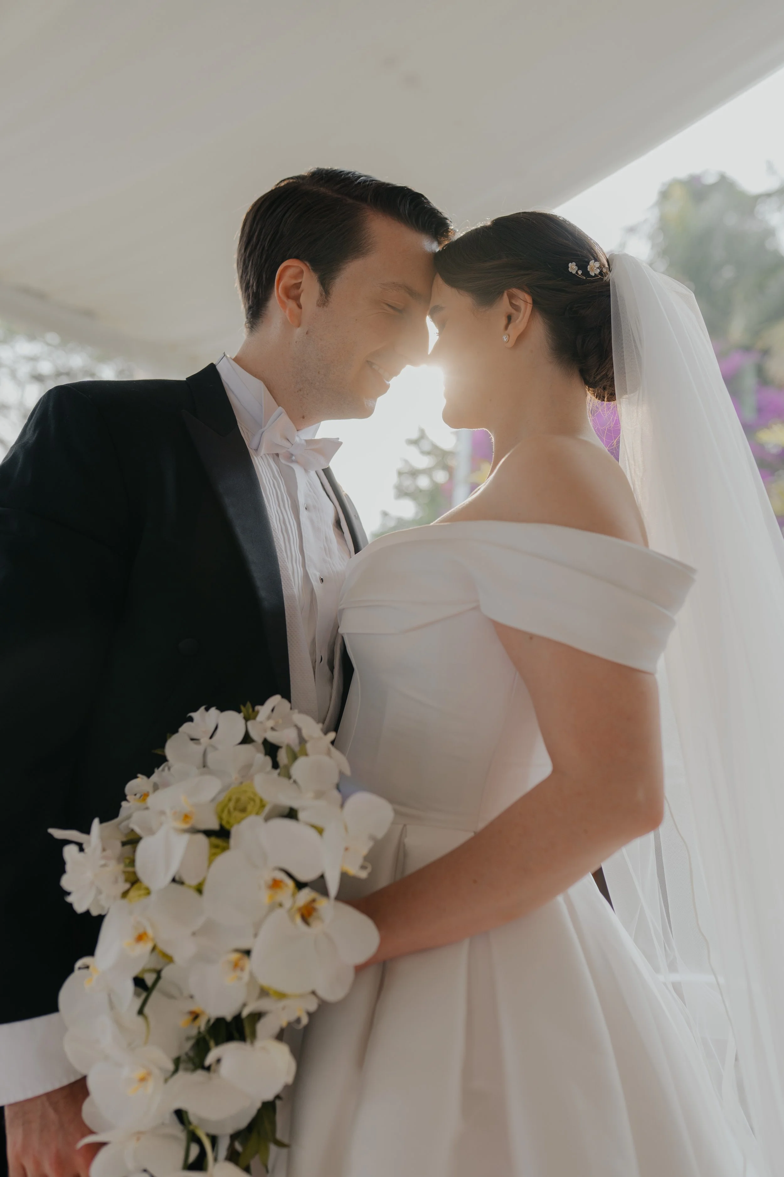 Una pareja de recién casados con la frente juntas, sonriendo y llenos de alegría en su boda.