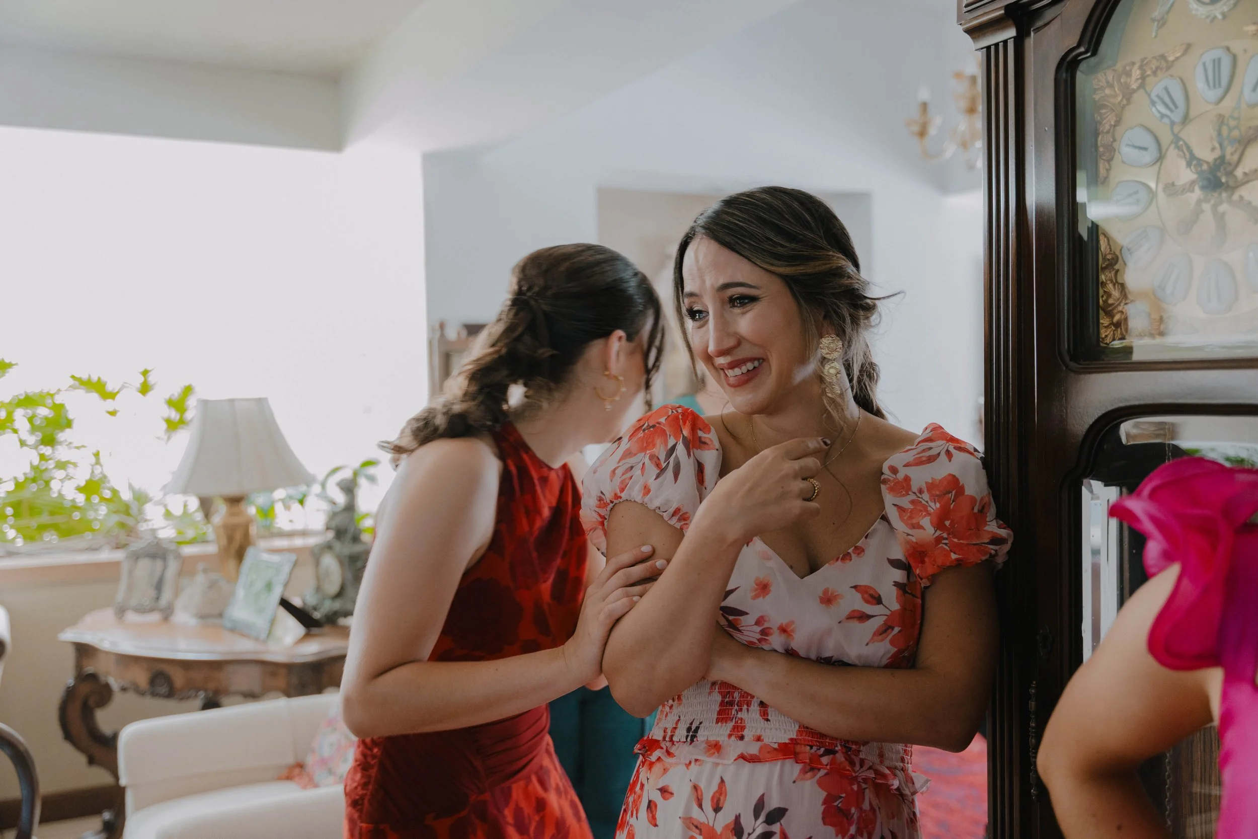 Dos mujeres compartiendo un momento emocional en una sala decorada con fotografías y muebles clásicos.