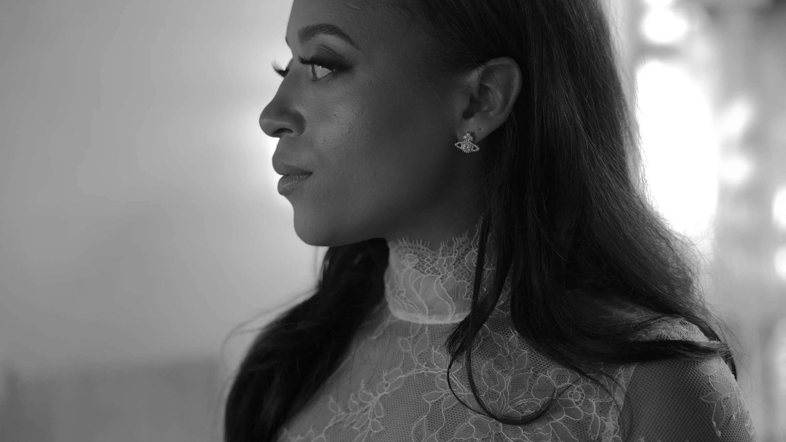 Retrato en blanco y negro de una mujer vista de perfil, con pendientes y un vestido de encaje, con cabello largo y oscuro.