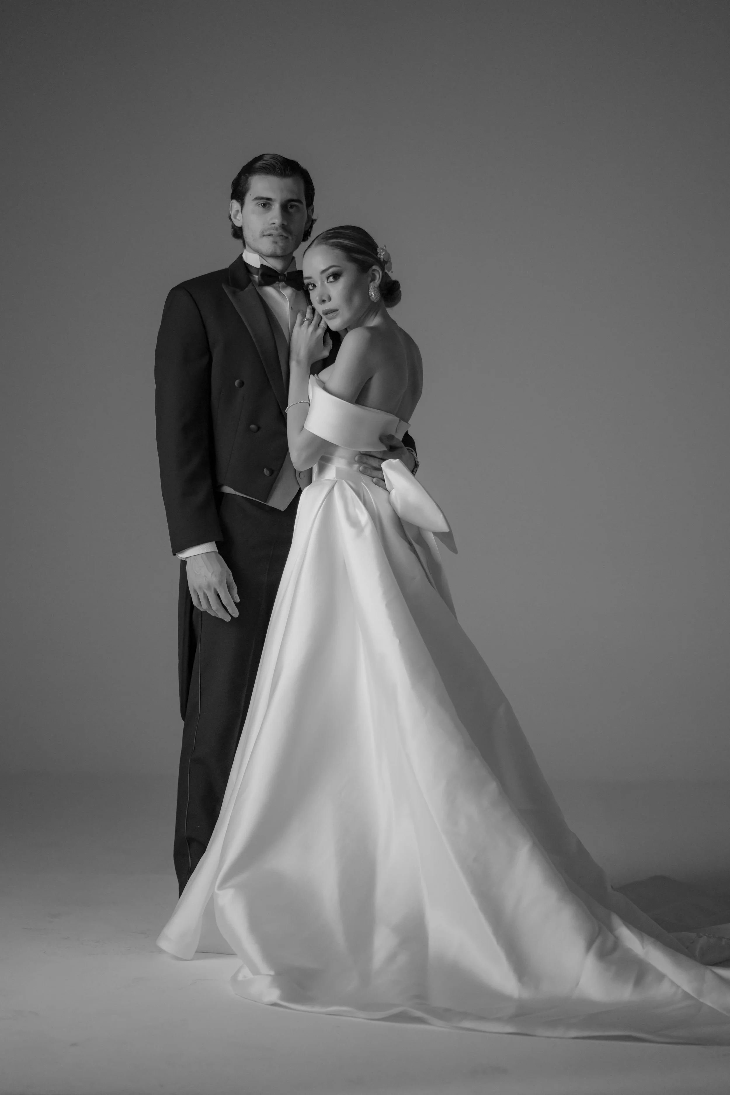 Retrato en blanco y negro de una pareja vestida de boda, con fondo gris liso.