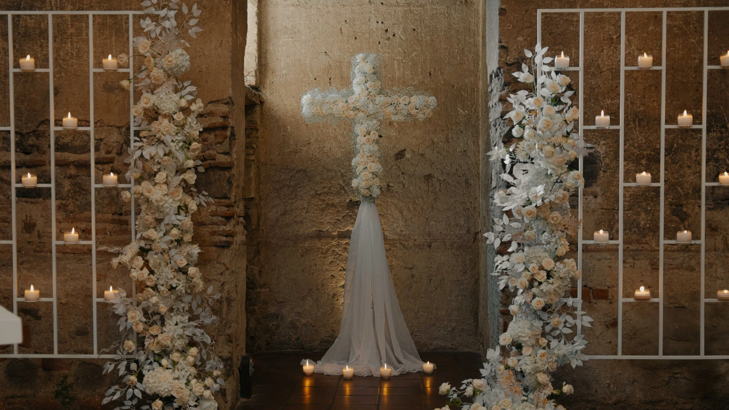 Altar de iglesia con cruz decorada con flores blancas y velas.