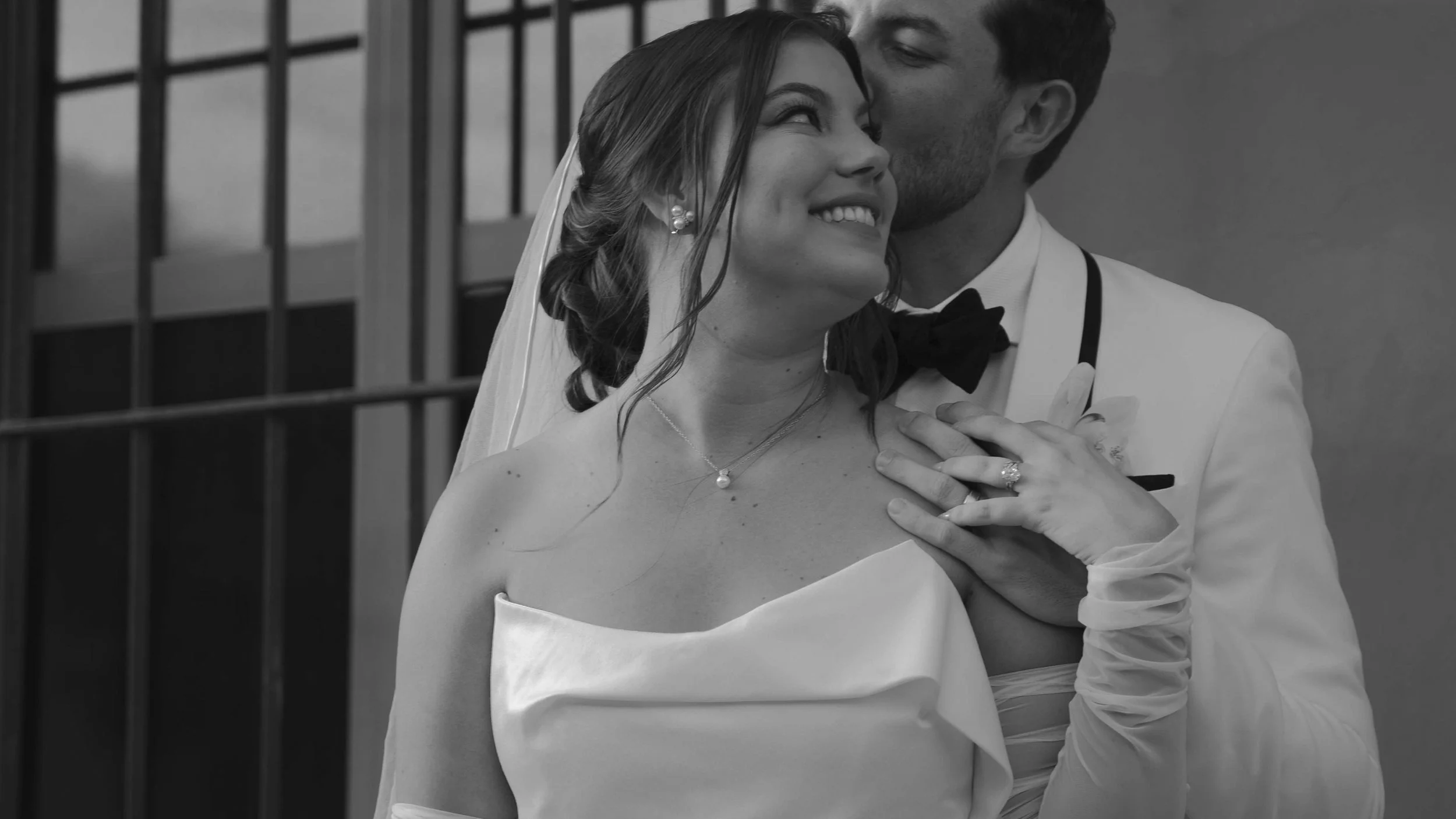 Una pareja en su boda, la mujer con vestido blanco y el hombre con traje formal, compartiendo un momento cercano y feliz.