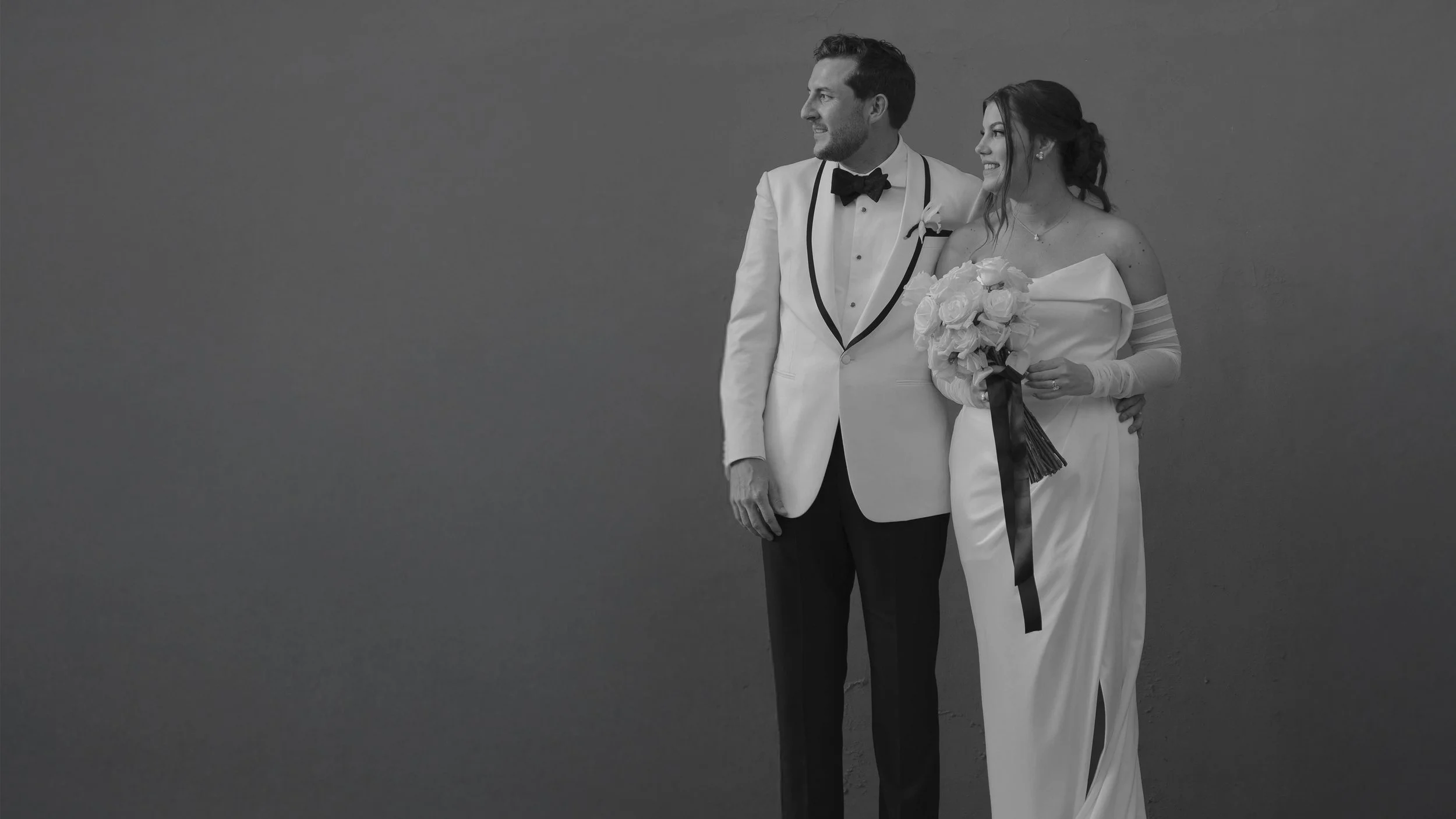 Pareja de recién casados en traje de boda posando juntos, la mujer sostiene un ramo de flores