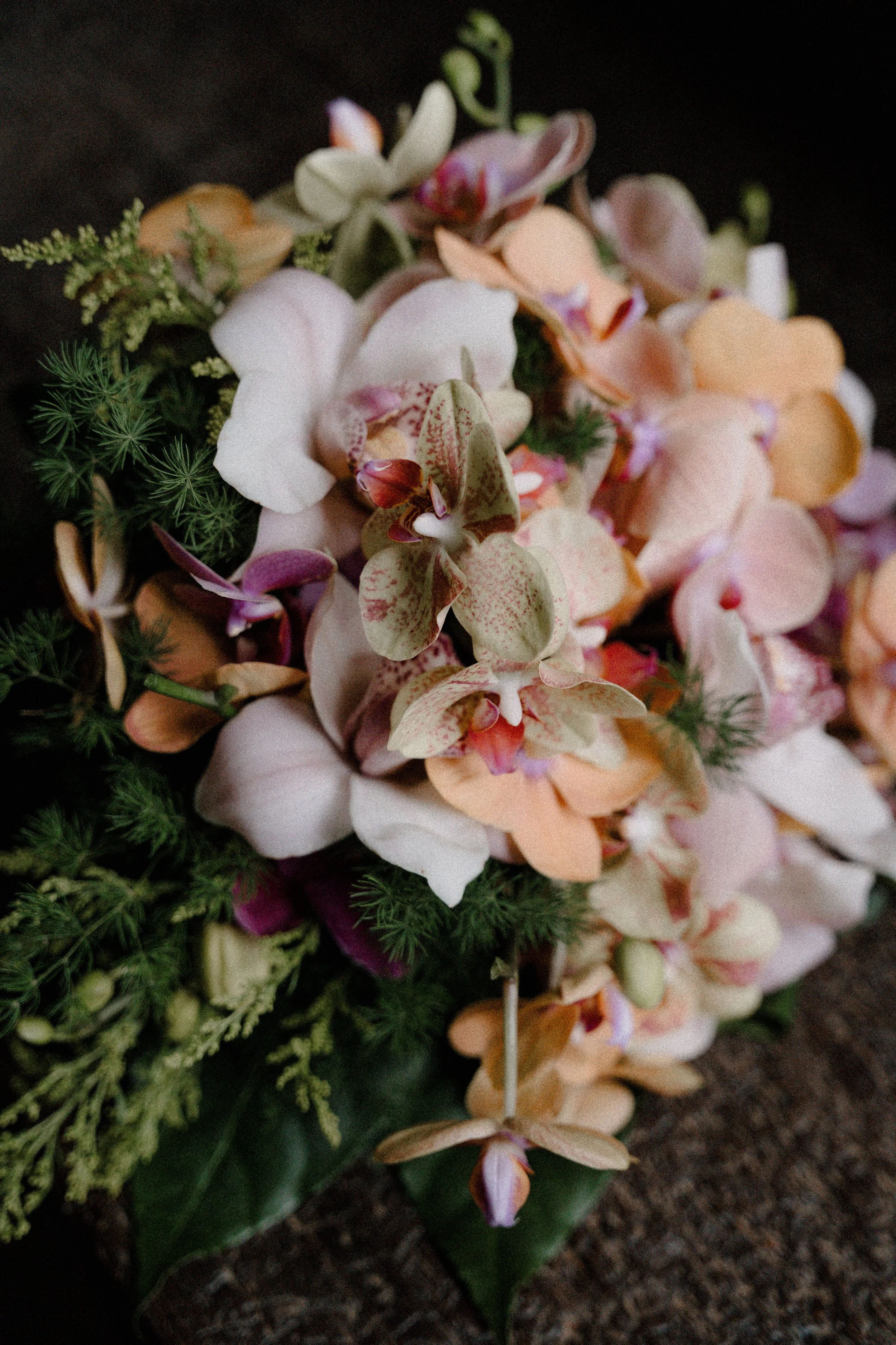 Ramo de flores con orquídeas de diversos colores, predominantemente en tonos rosados, blancos, y verdes, con hojas verdes y follaje ornamental.