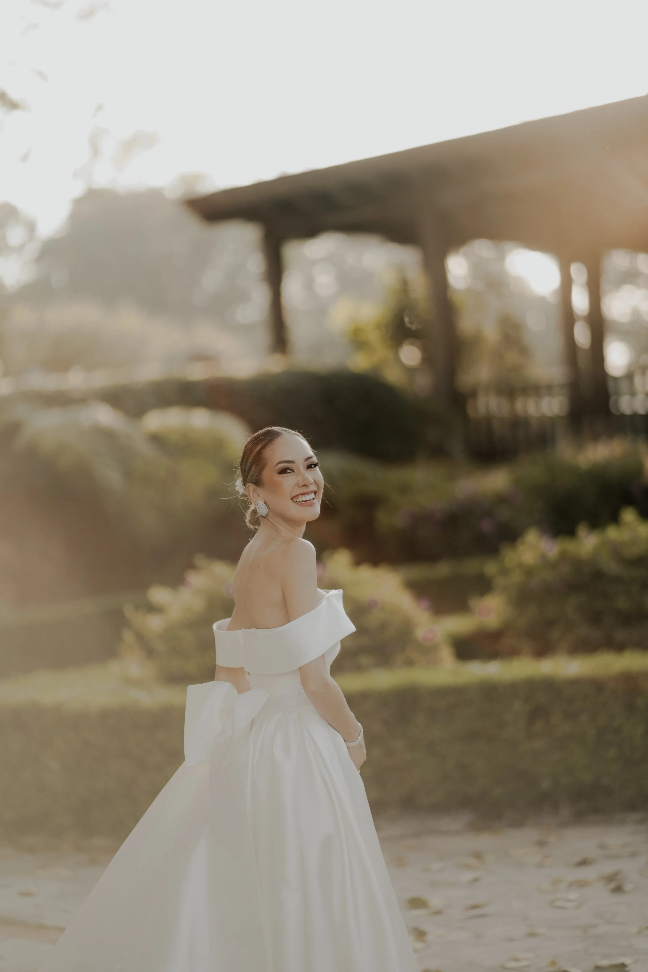 Una mujer con vestido de novia sonriendo en un jardín al atardecer.