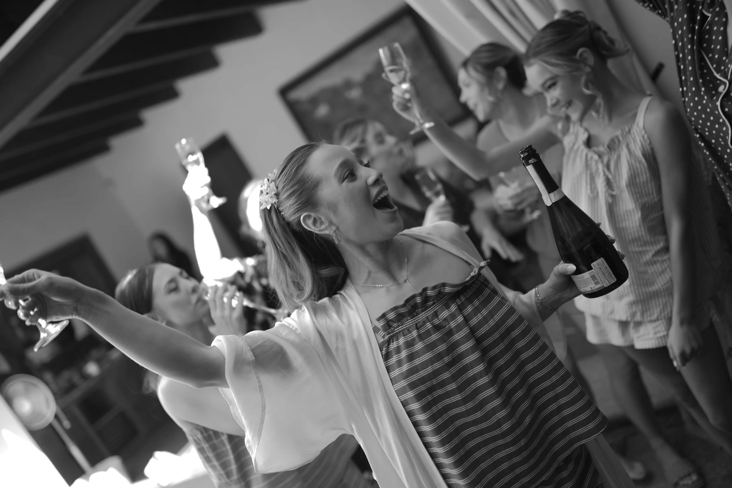 Grupo de mujeres celebrando con copas de vino y una botella en un ambiente festivo.