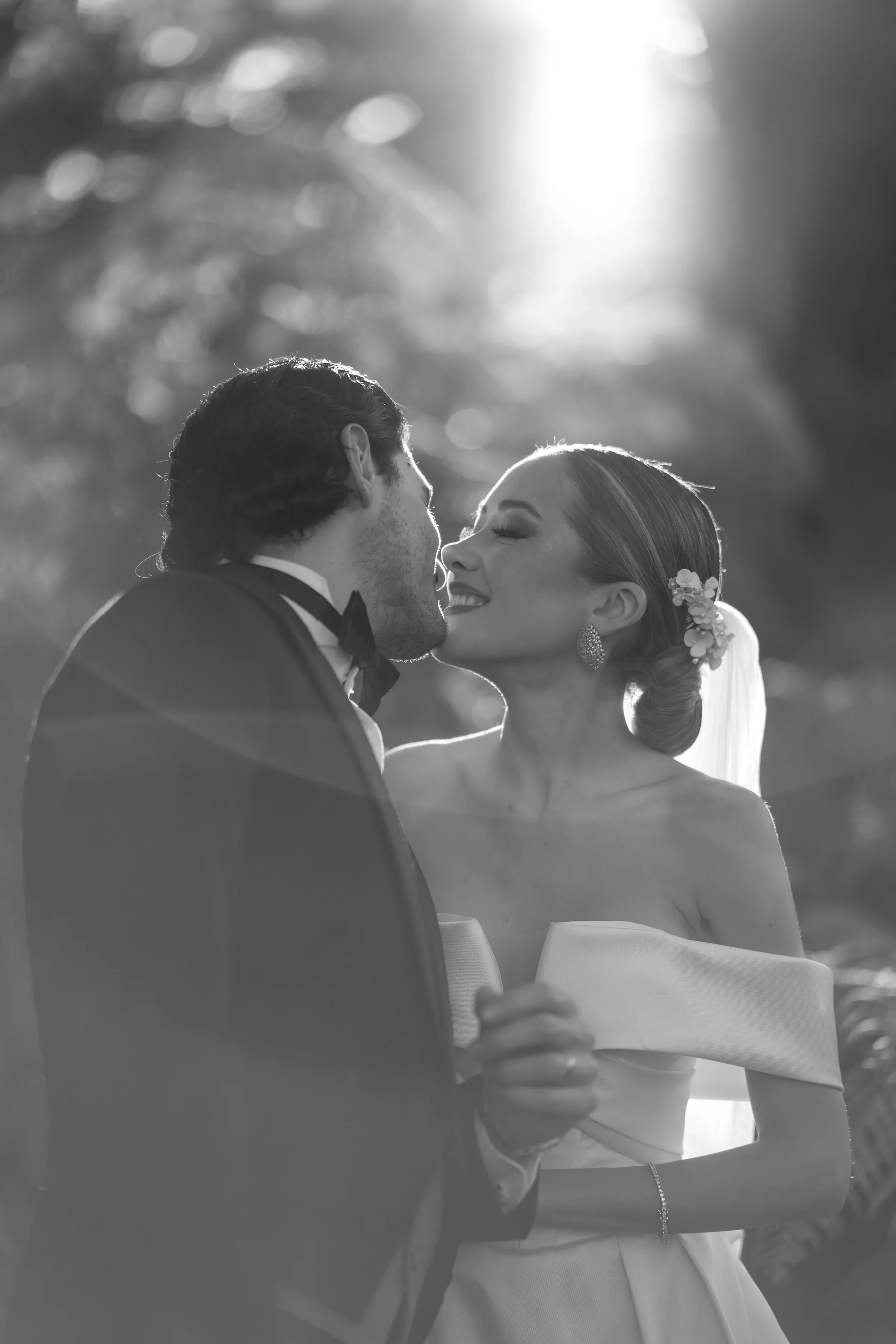 Pareja de novios en su boda, la novia y el novio se están besando en un entorno natural con luz suave y un fondo difuso.
