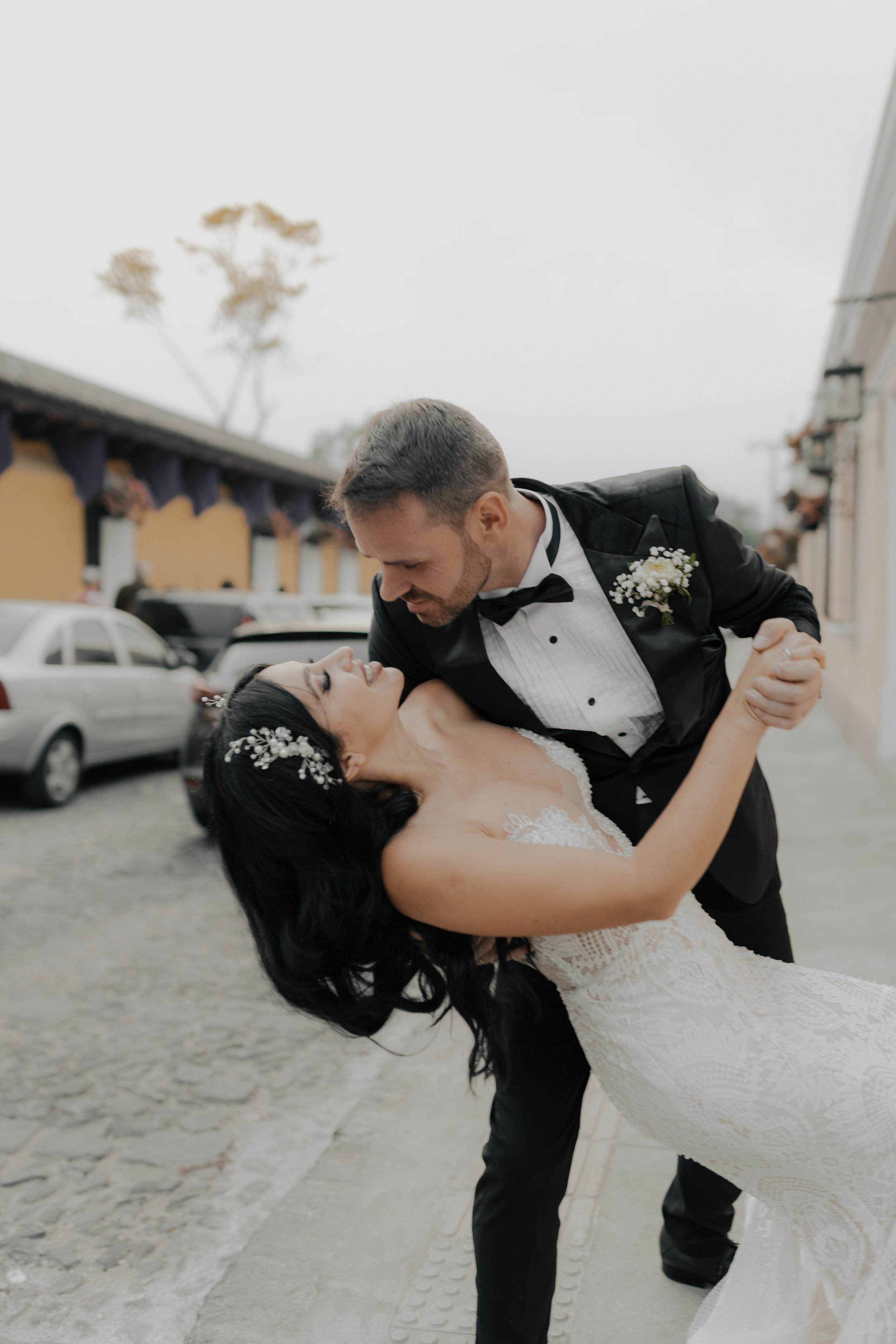Pareja de recién casados bailando en la calle, el hombre la sostiene en un abrazo y se miran con cariño.