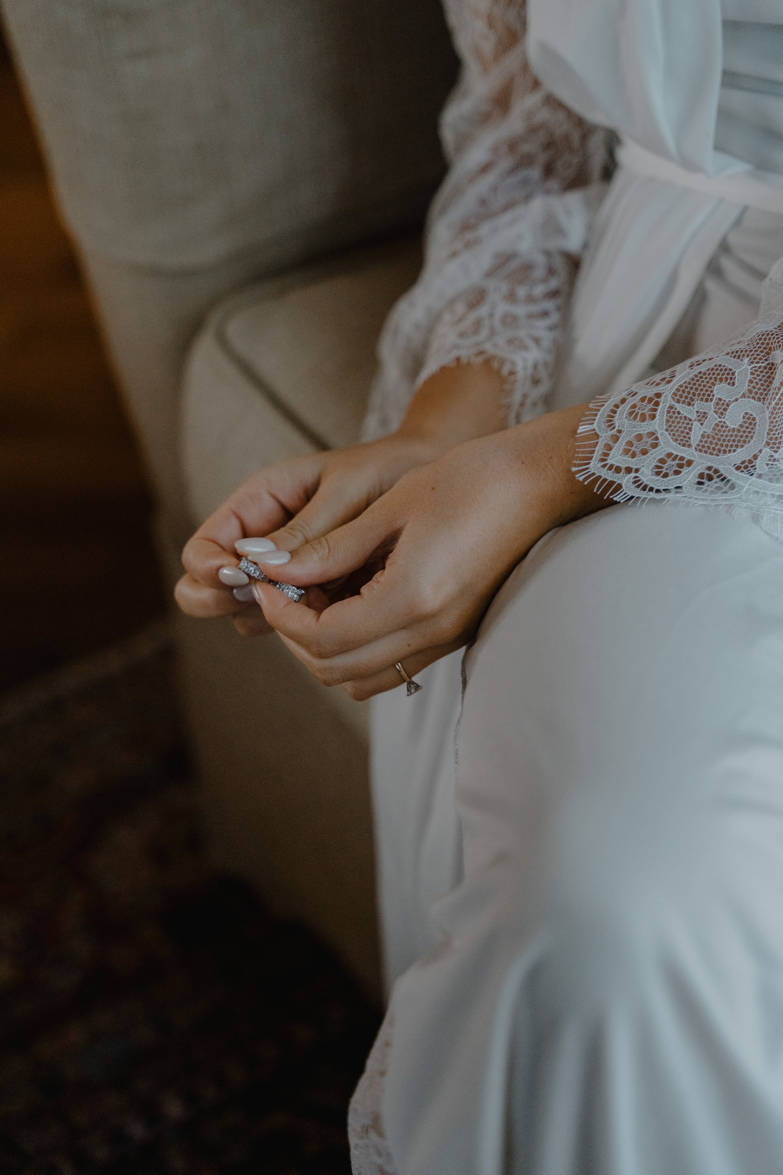 Muñeca con anillo de compromiso en manos de una mujer que lleva un vestido de encaje y satén blanco.