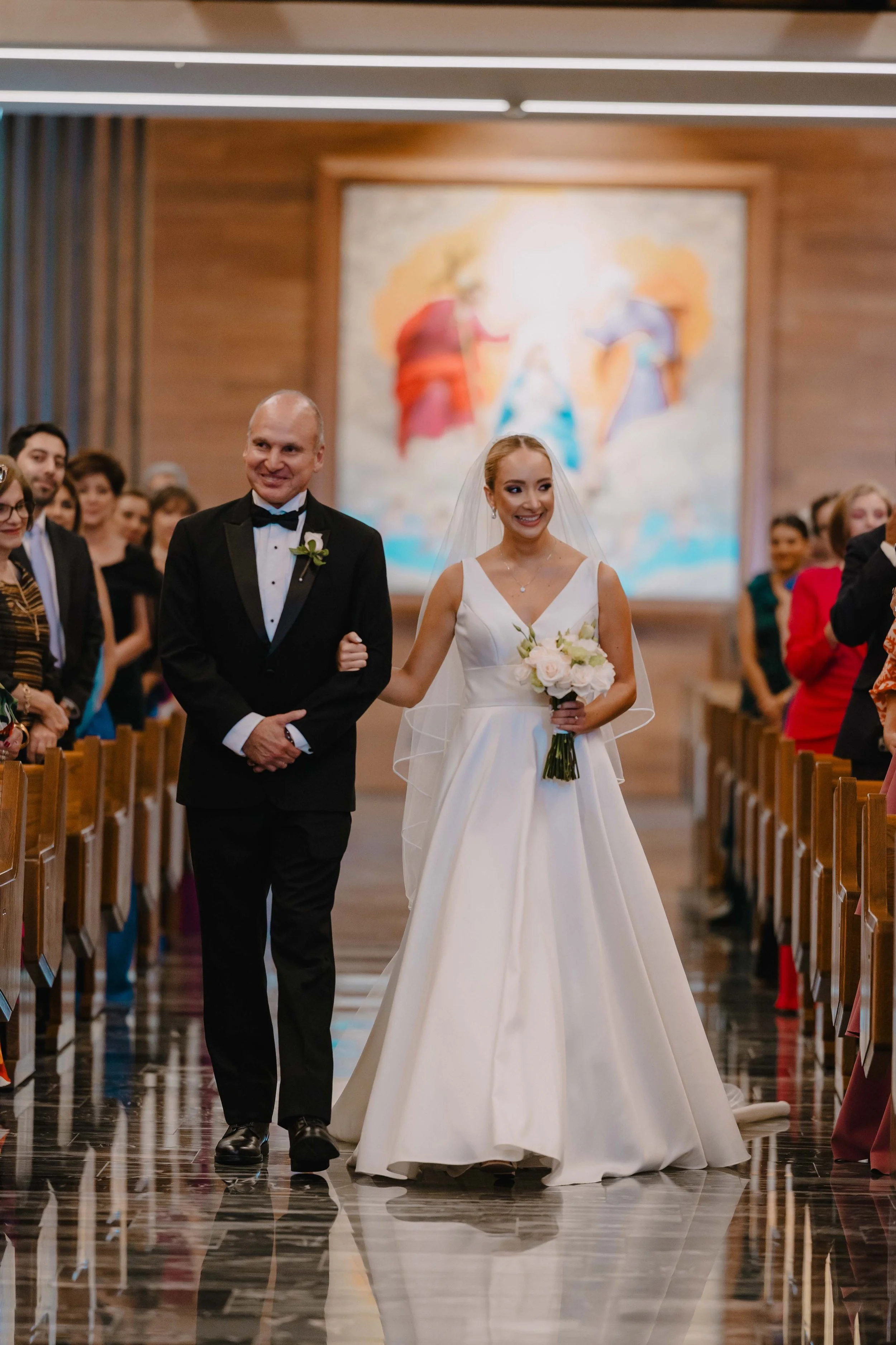 Novia y padre caminando por pasillo de iglesia en su boda con los invitados a los lados.