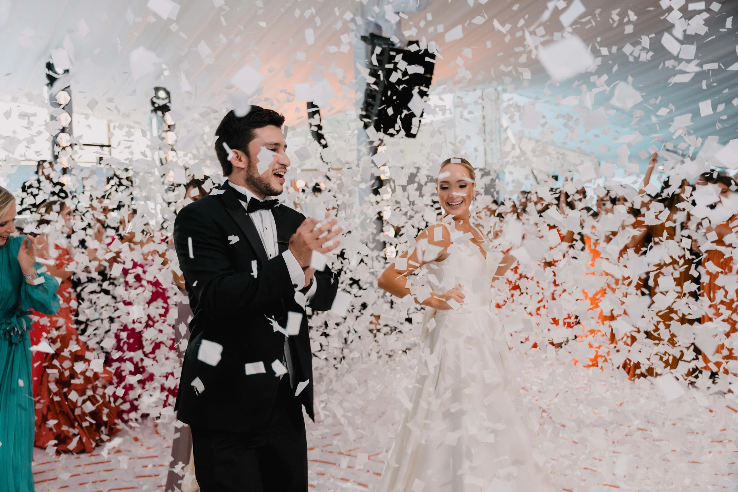 Pareja de recién casados celebrando con confeti en una fiesta de bodas, rodeados de invitados alegres.