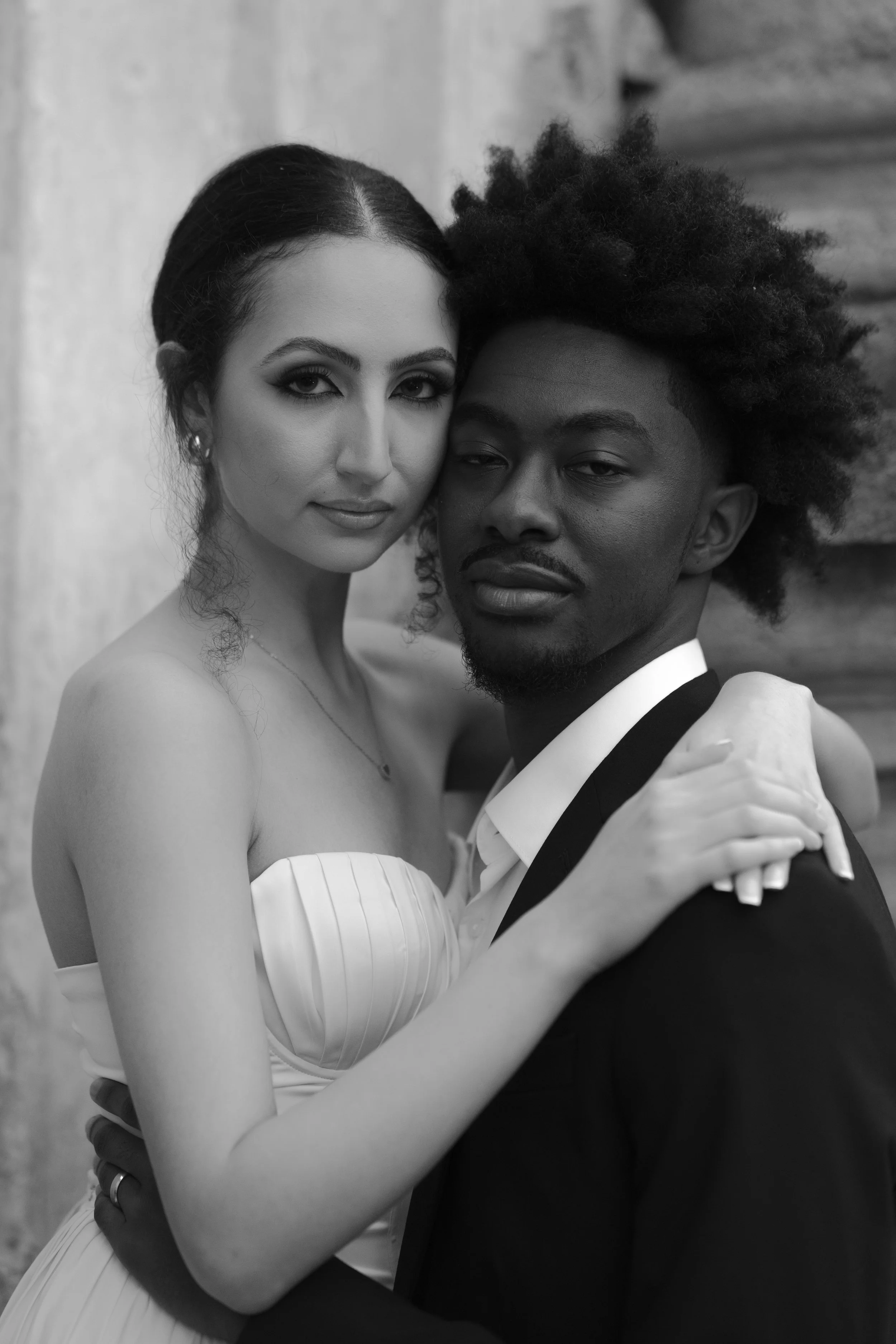 una pareja en un retrato en blanco y negro, ella con vestido de novia y él con traje de novio, abrazándose