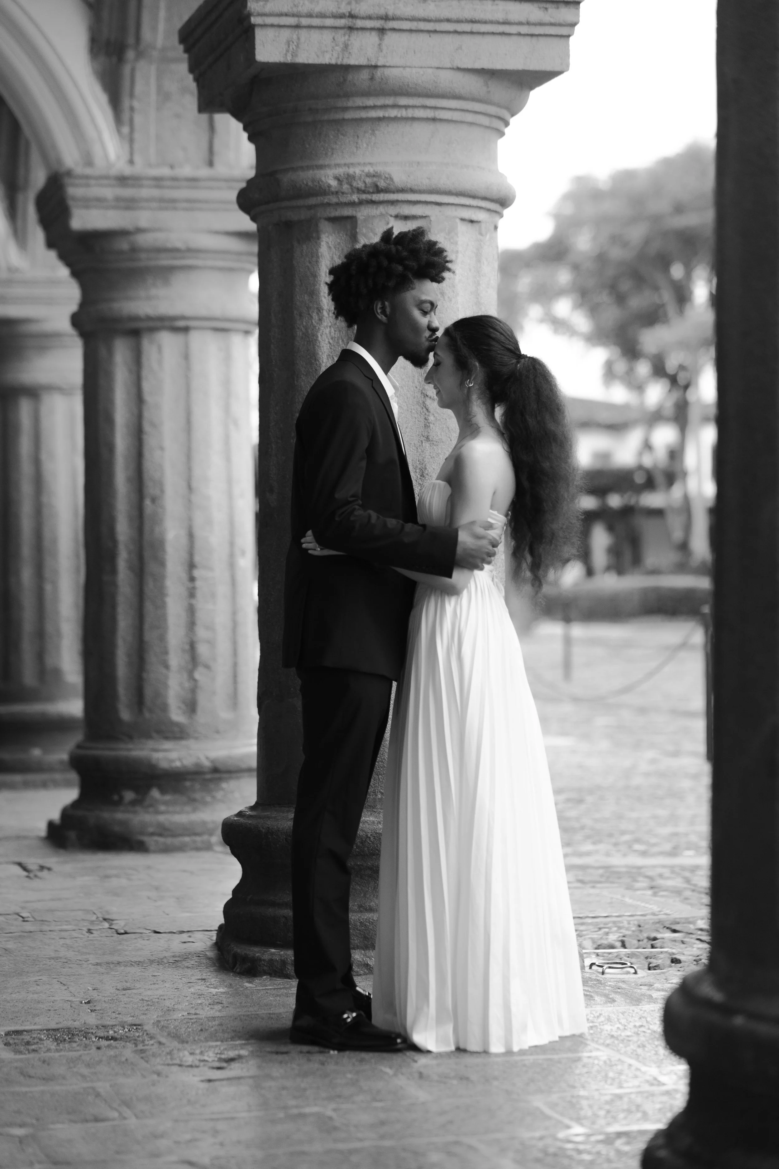 Pareja de novios en un abrazo romántico bajo columnas, en una fotografía en blanco y negro, en un entorno arquitectónico clásico.