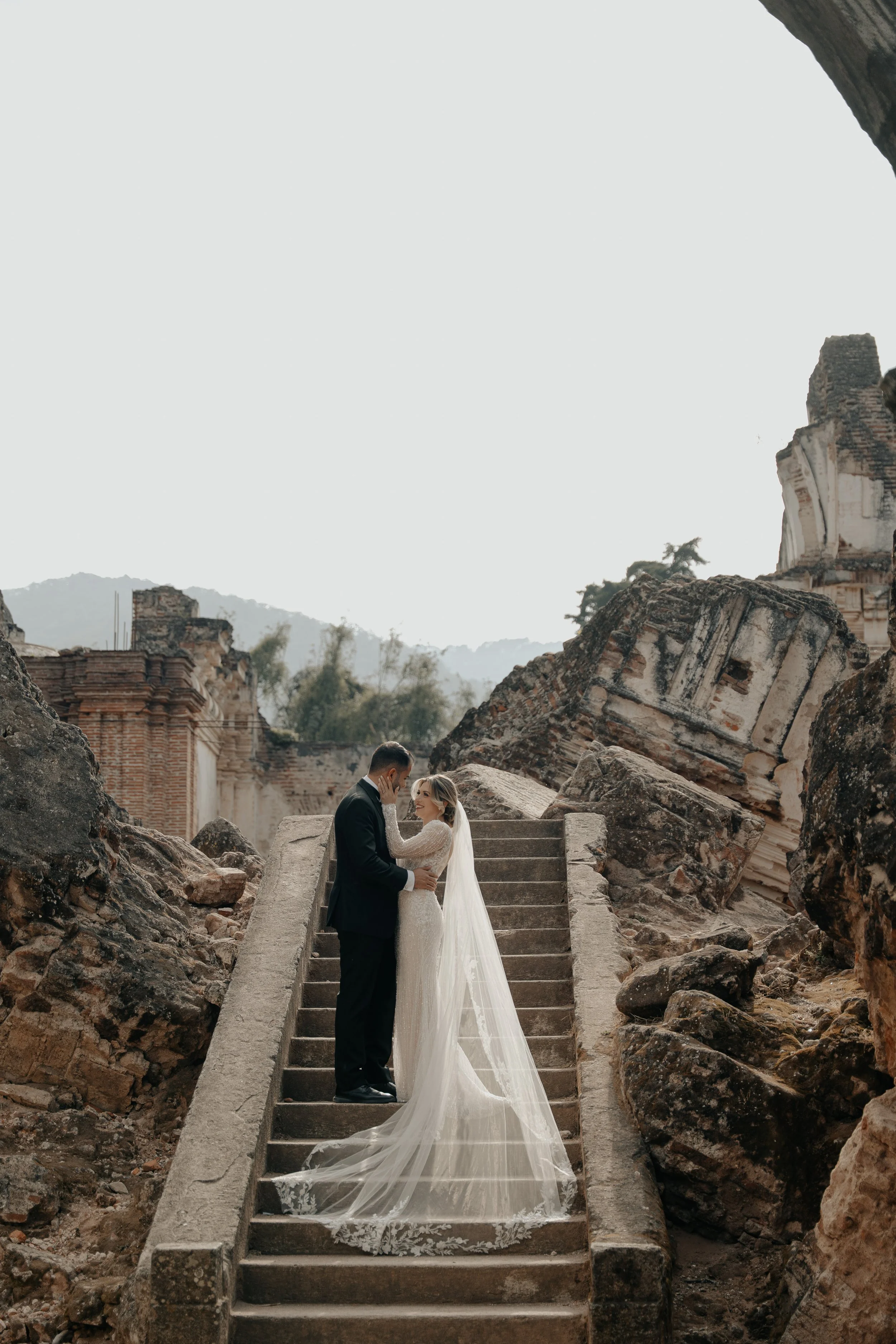 Pareja de boda abrazándose en unas escaleras rodeadas de ruinas antiguas.