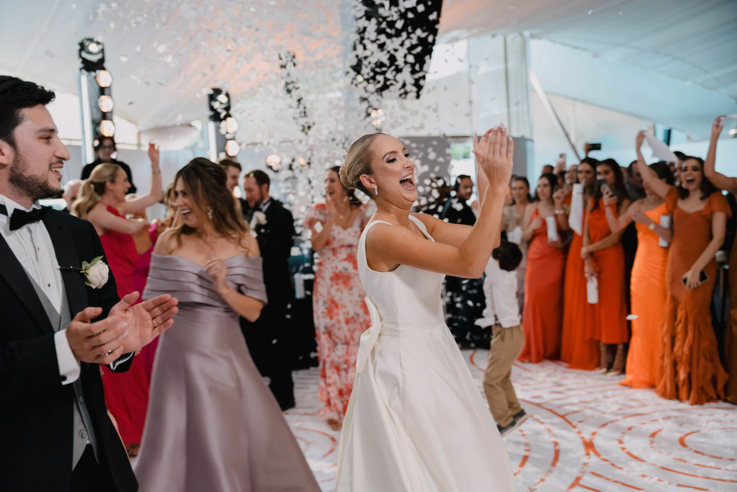 Pareja de boda bailando feliz con invitados celebrando y lanzando confeti en un salón decorado elegantes.