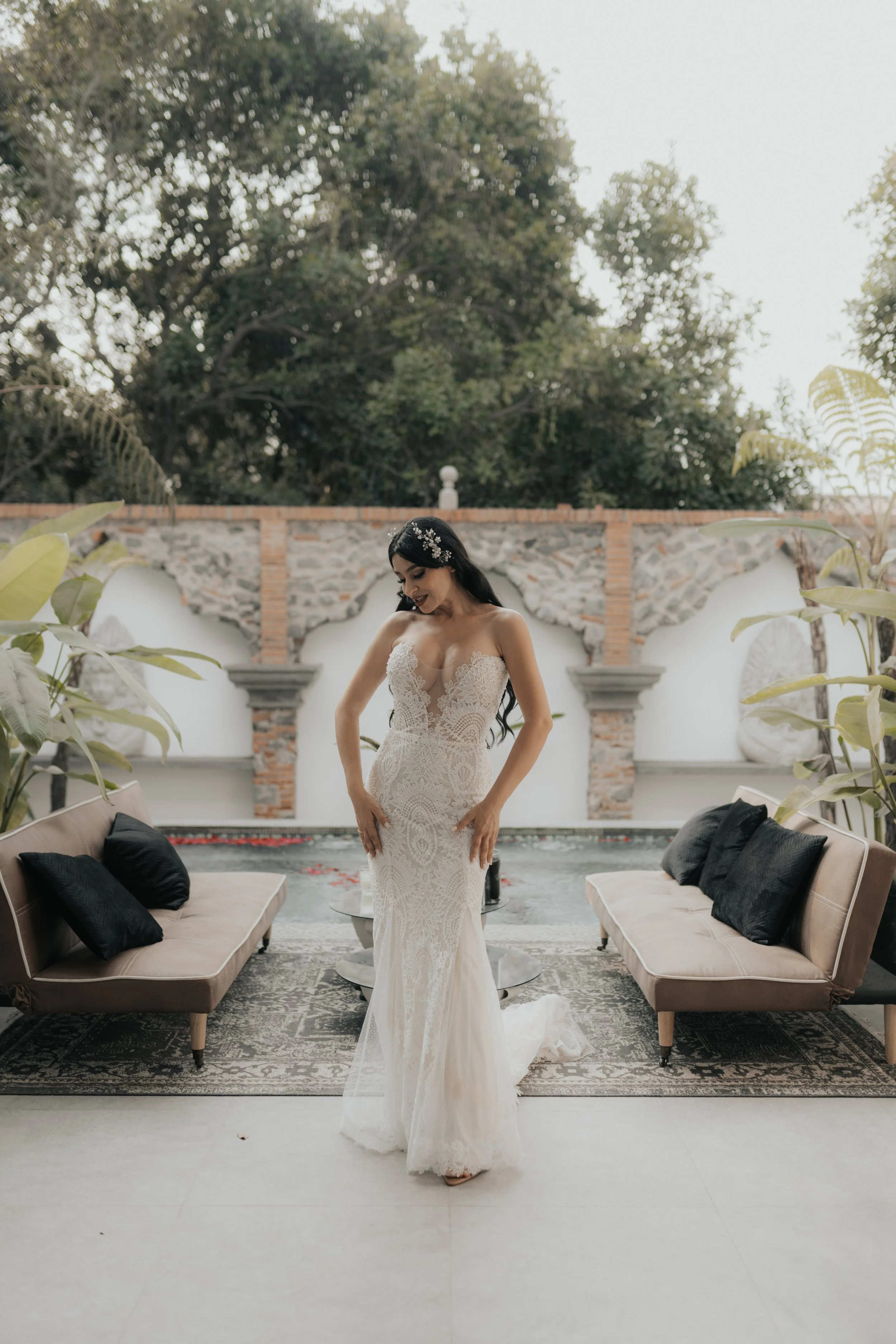 Una novia en vestido de boda blanco con fondo de pared de piedra y vegetación.
