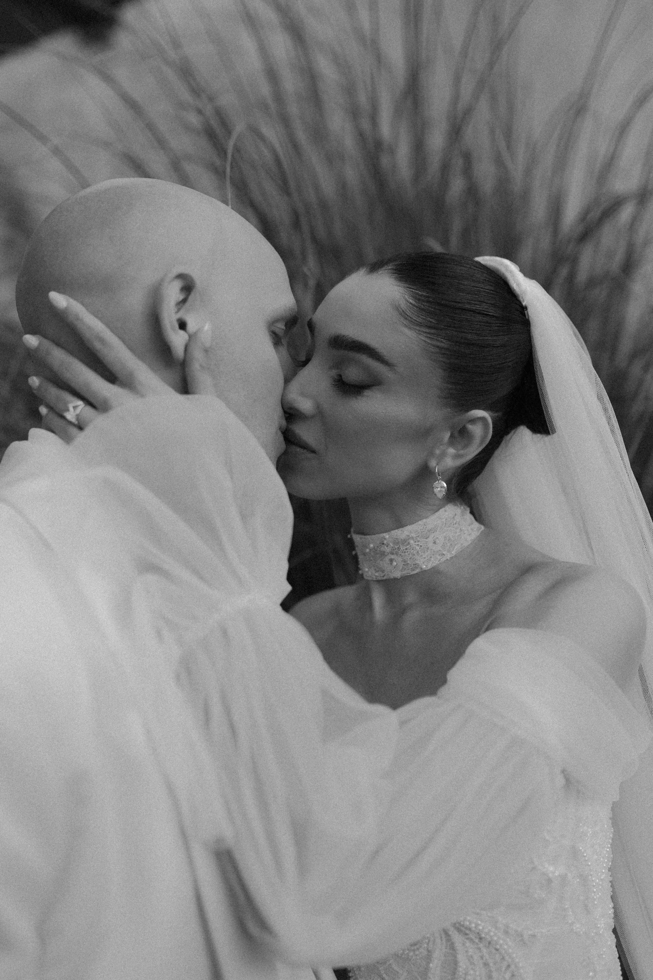 Una pareja en una boda, en un momento romántico, compartiendo un beso con los ojos cerrados, ella con velo y vestido de novia, él con ropa formal.