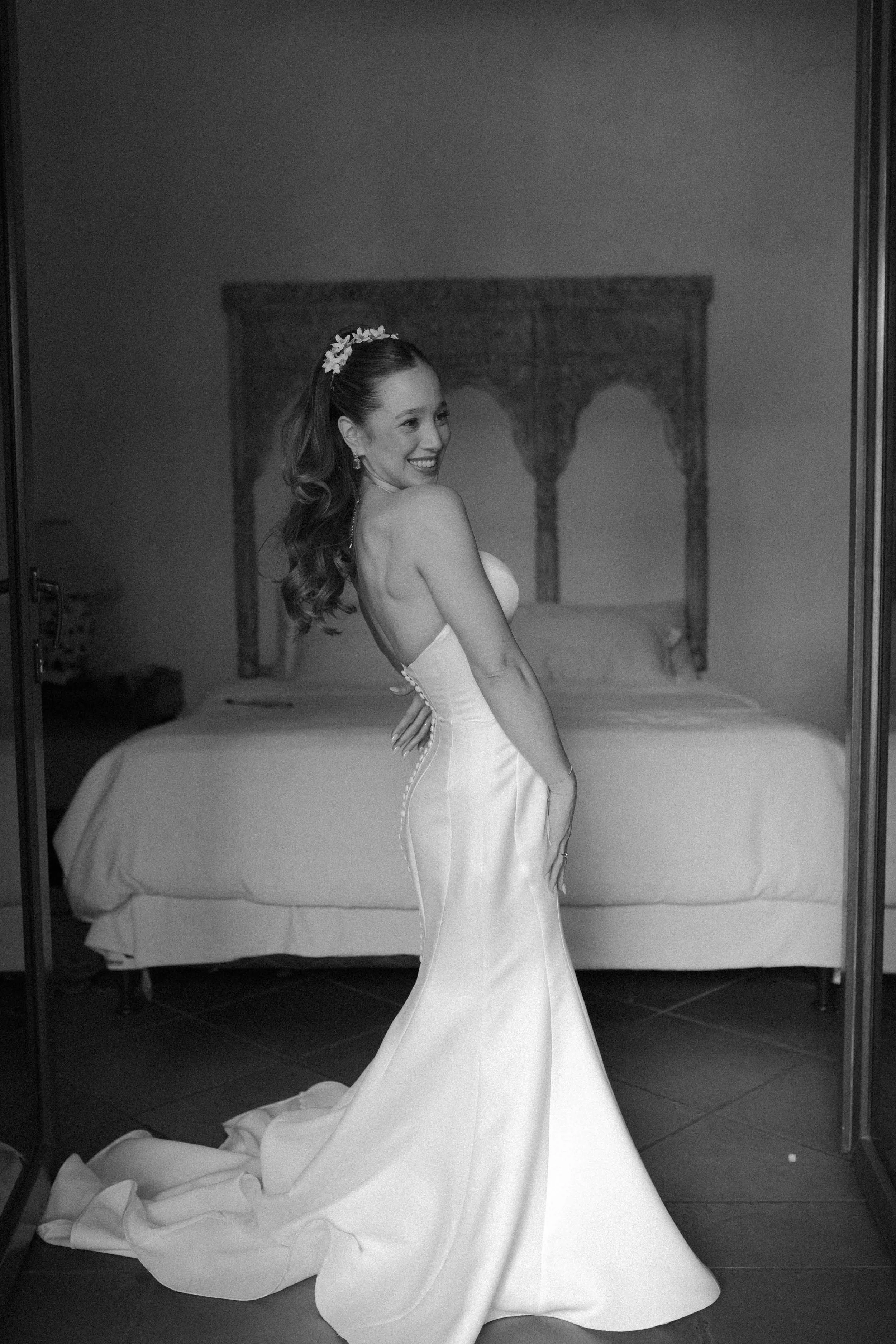 Mujer en vestido de novia sonriendo en una habitación, de espaldas en un espejo.
