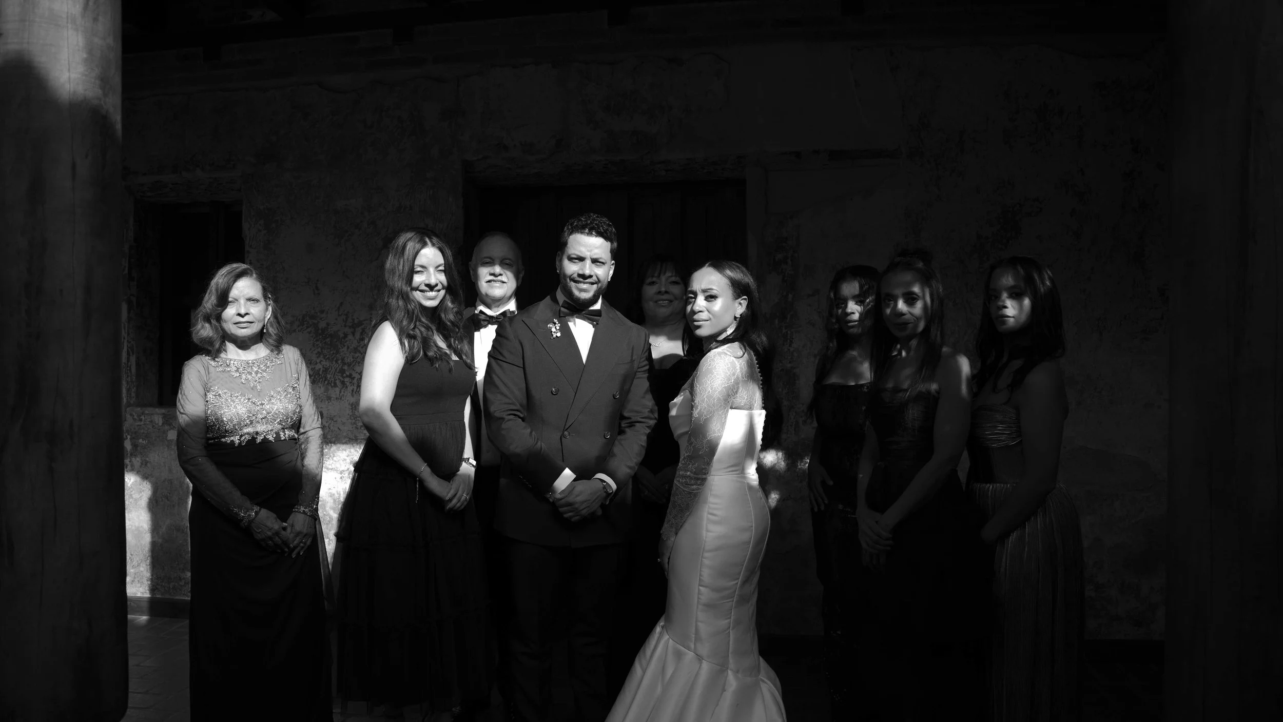 Grupo de personas en un evento formal, incluyendo un hombre y una mujer en el centro, rodeados de otras mujeres, en un entorno oscuro.