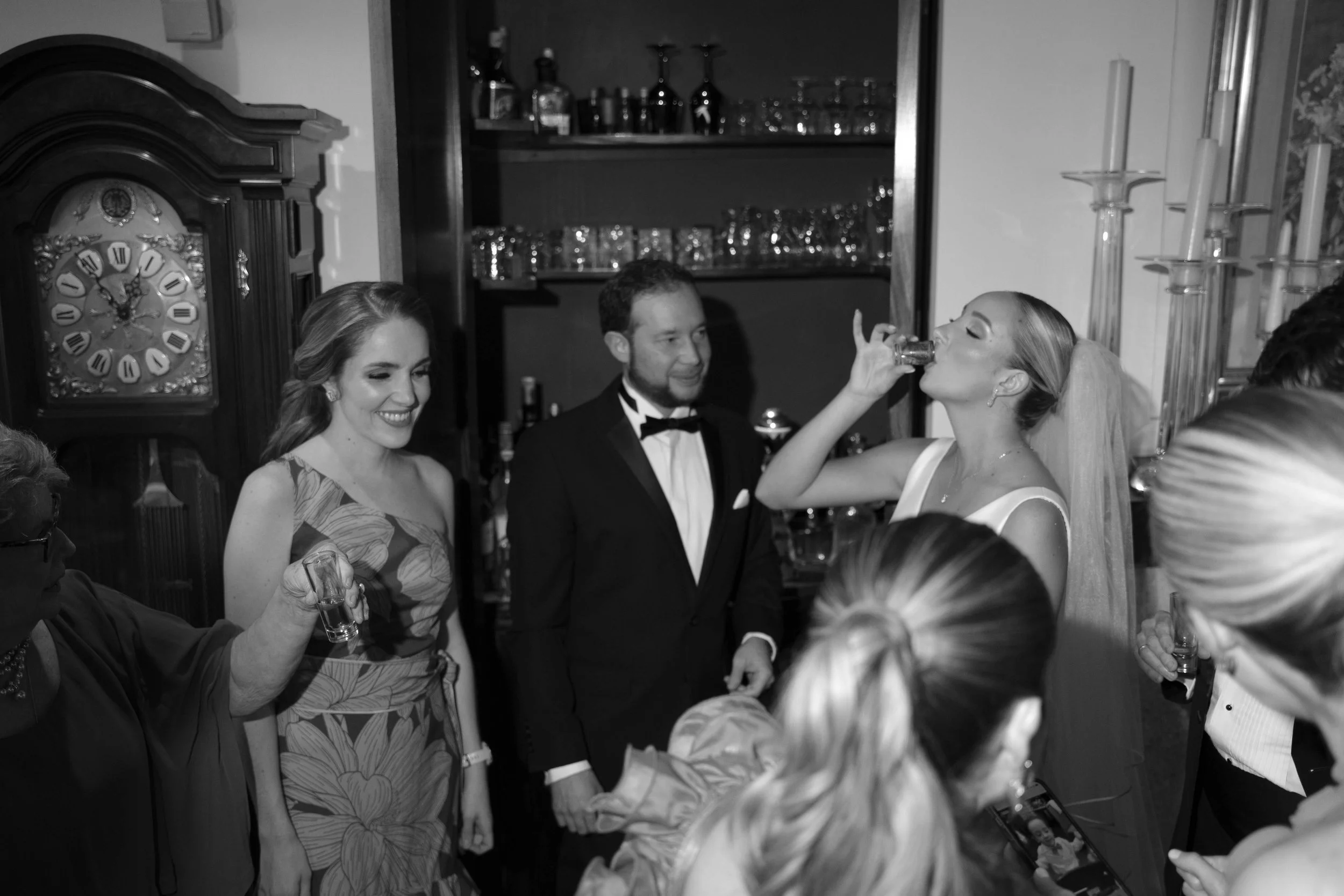 Grupo de personas en celebración, con una mujer bebiendo un trago, en un ambiente de fiesta elegante