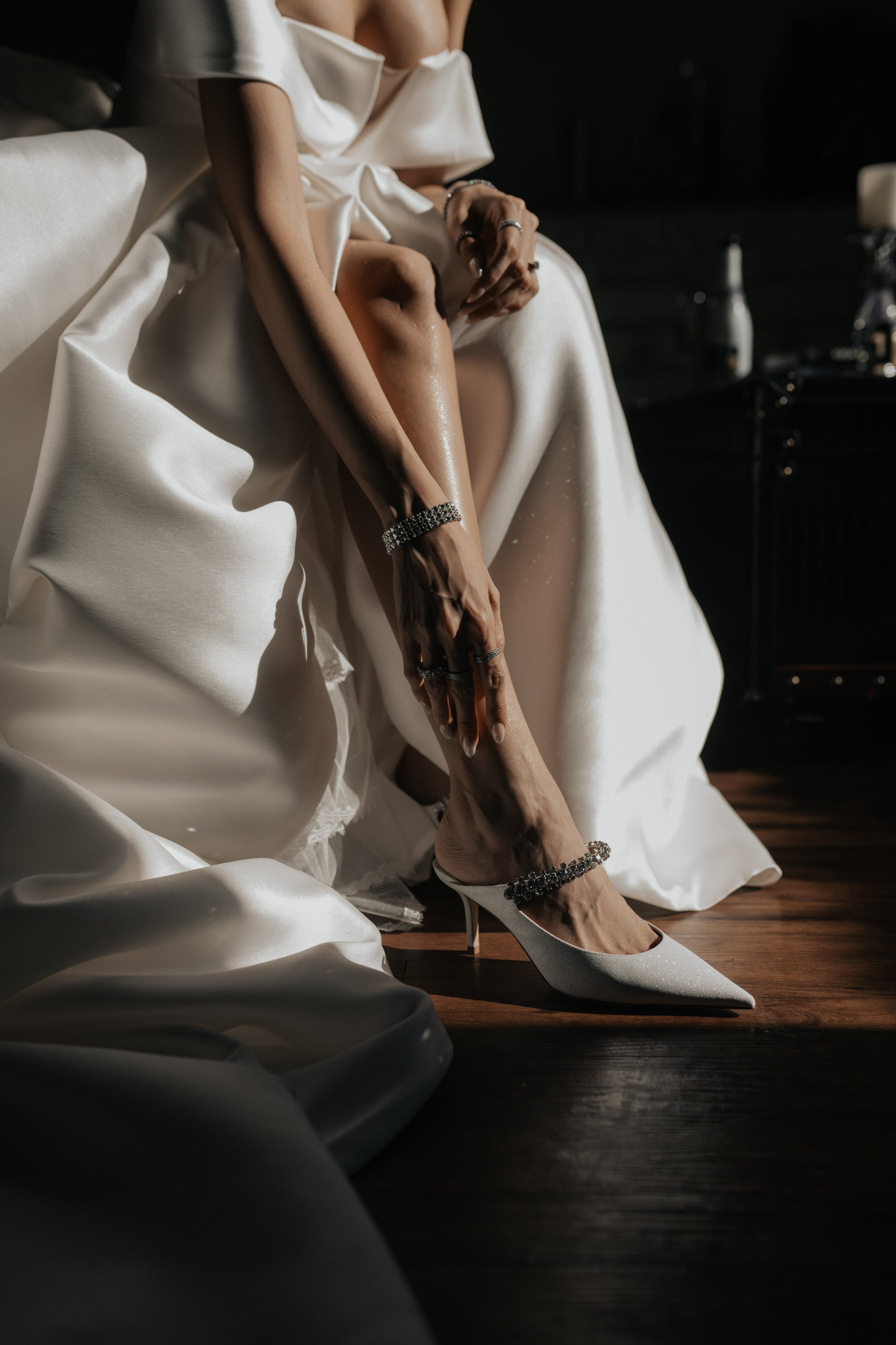 Mujer en vestido de novia ajustando su tacón alto blanco con accesorios brillantes.