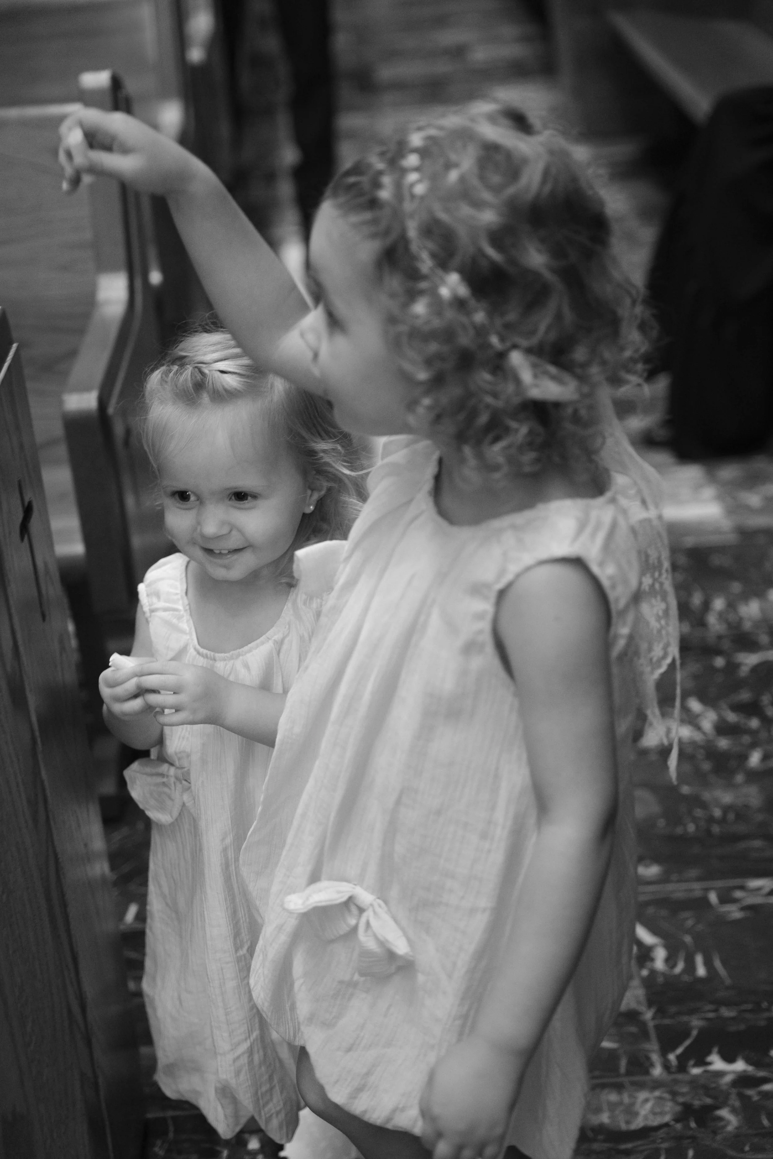 Dos niñas pequeñas juegan juntas, una tocando un poste y la otra sonriendo, en un ambiente interior.