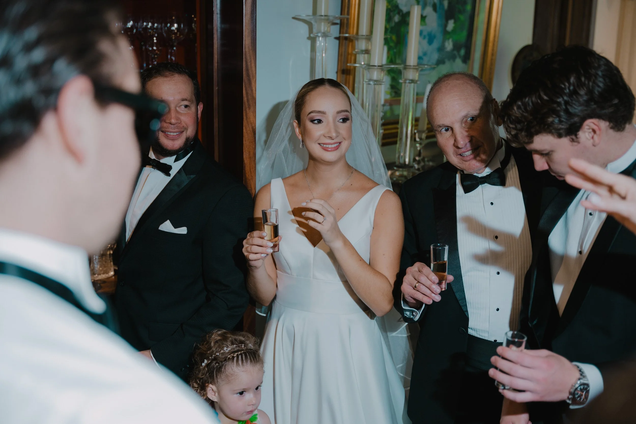 Grupo de personas en celebración de bodas con la novia en el centro, rodeada de hombres vestidos con esmoking y una niña pequeña en primer plano.