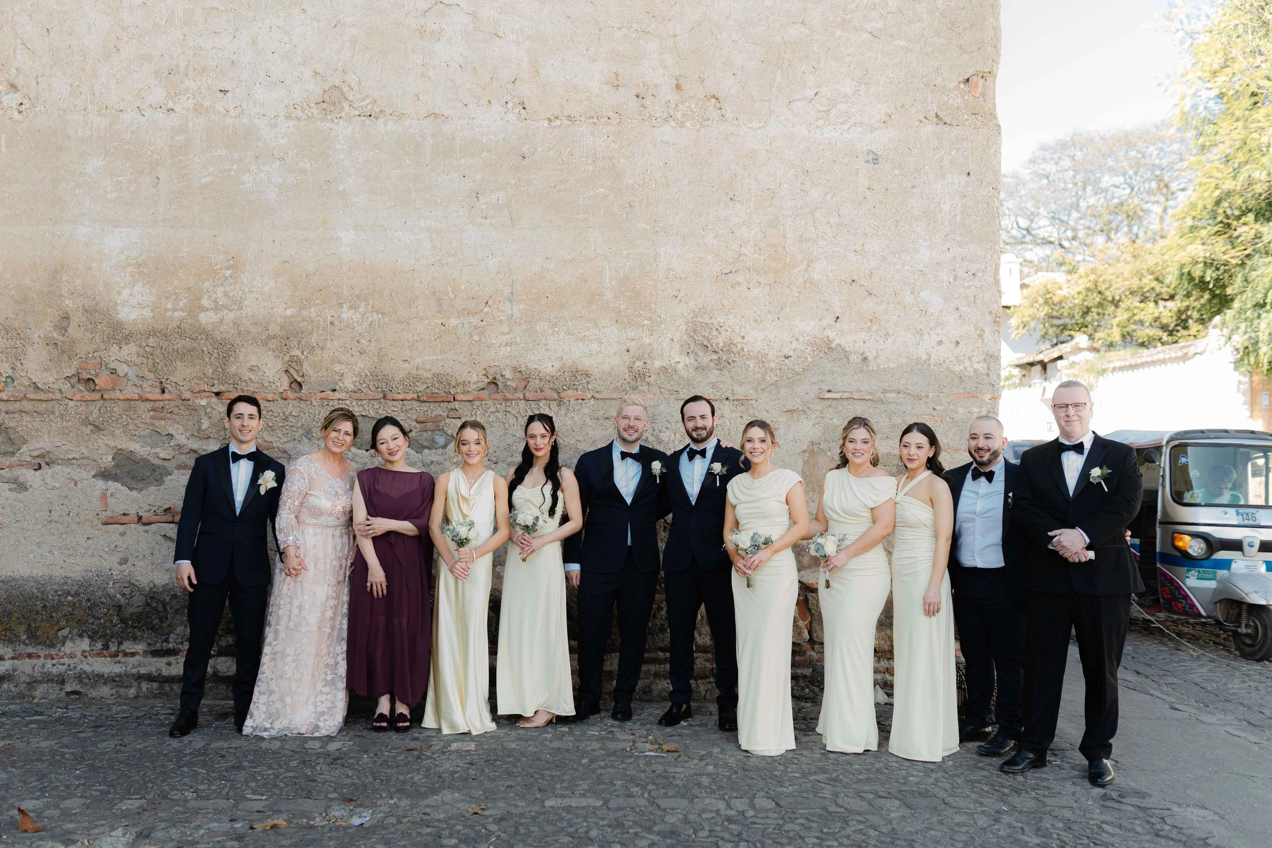 Grupo de personas en ropa formal de boda posando frente a una pared de ladrillos.