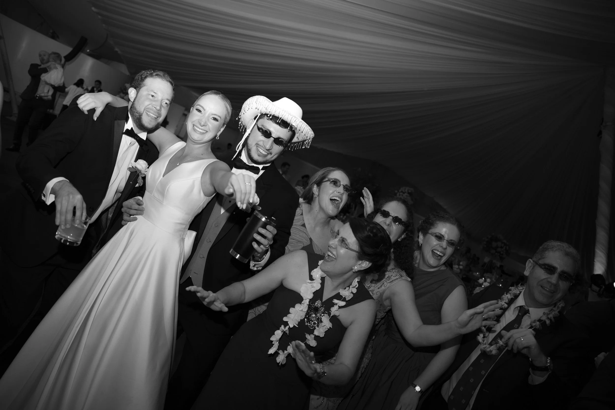 Grupo de personas celebrando en una fiesta, algunos con disfraces y accesorios divertidos, riendo y bailando en una fiesta formal