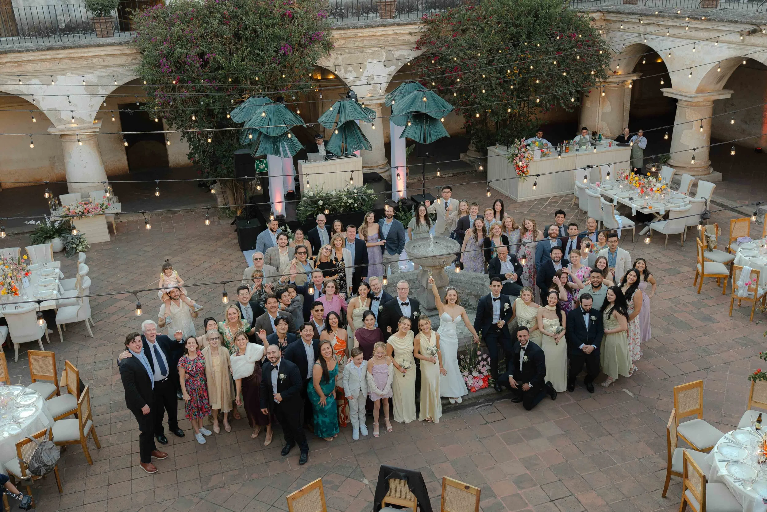 Grupo de personas en una boda en un patio con decoraciones florales y luces.