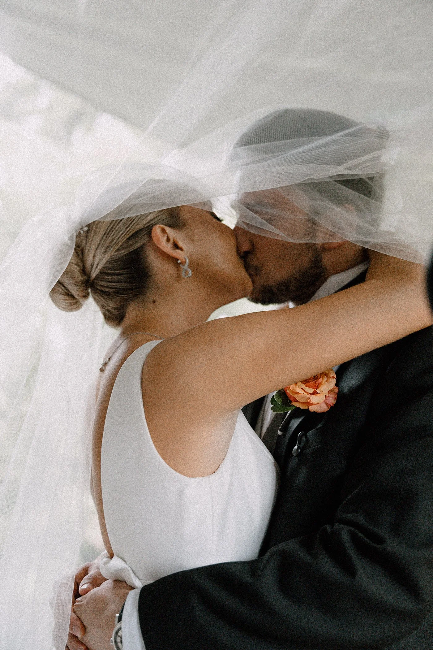 Una pareja de novios besándose, con un velo de novia cubriéndolos, en una boda en interiores.