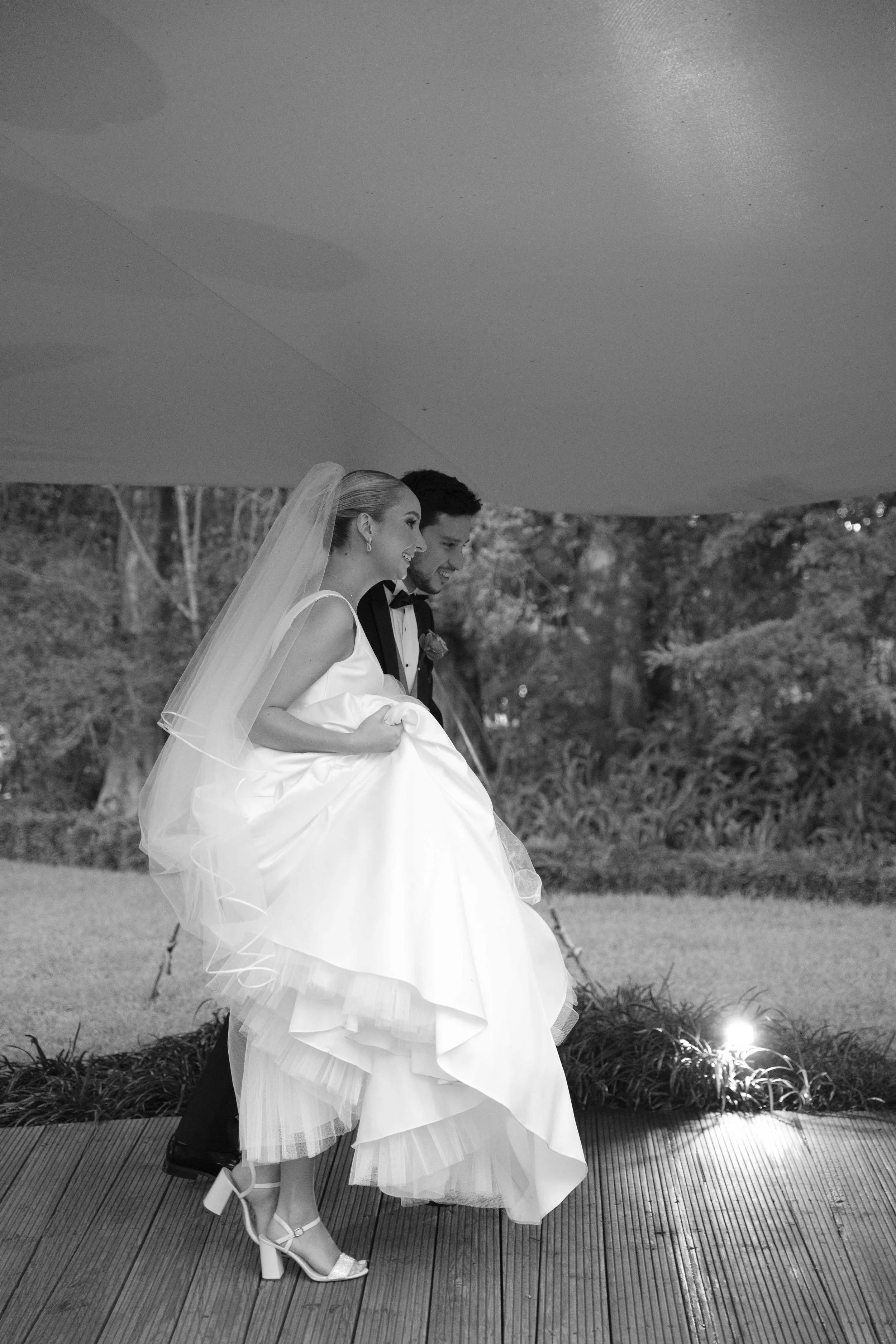 Pareja de recién casados, la novia en vestido largo y velo, el novio en traje de etiqueta, caminando de la mano en un entorno natural durante su boda.