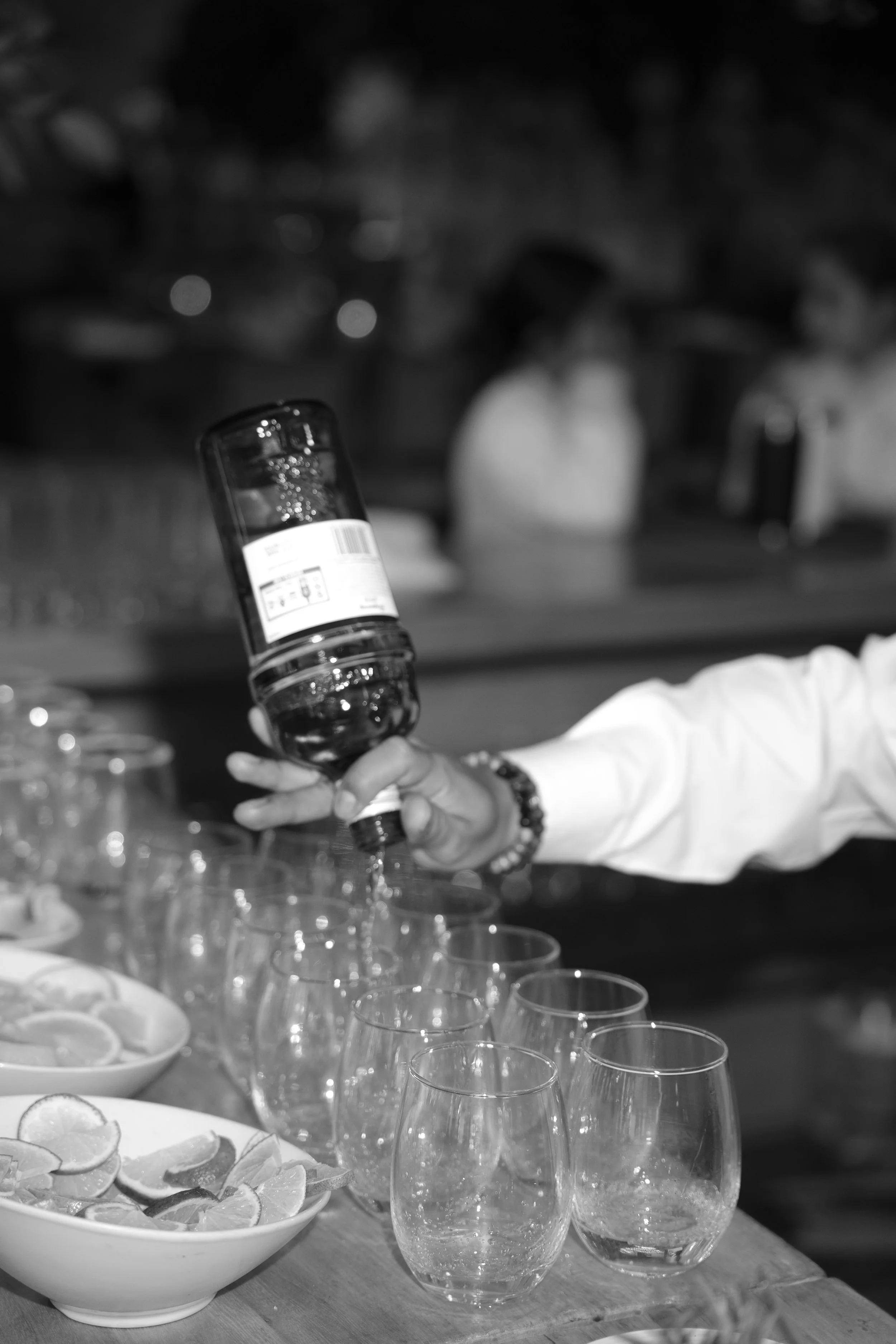 Persona sirviendo agua de una botella en copas, con platos de limones en la mesa.