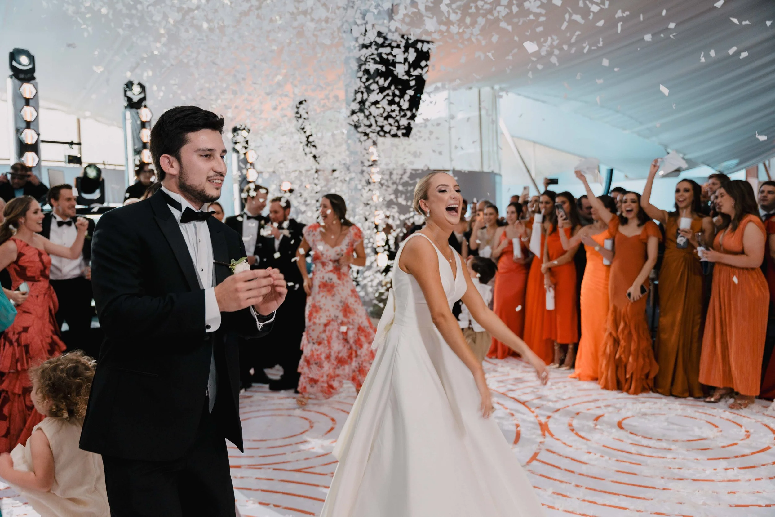 Pareja de recién casados bailando en su boda, rodeados de invitados que celebran con confeti y risas.