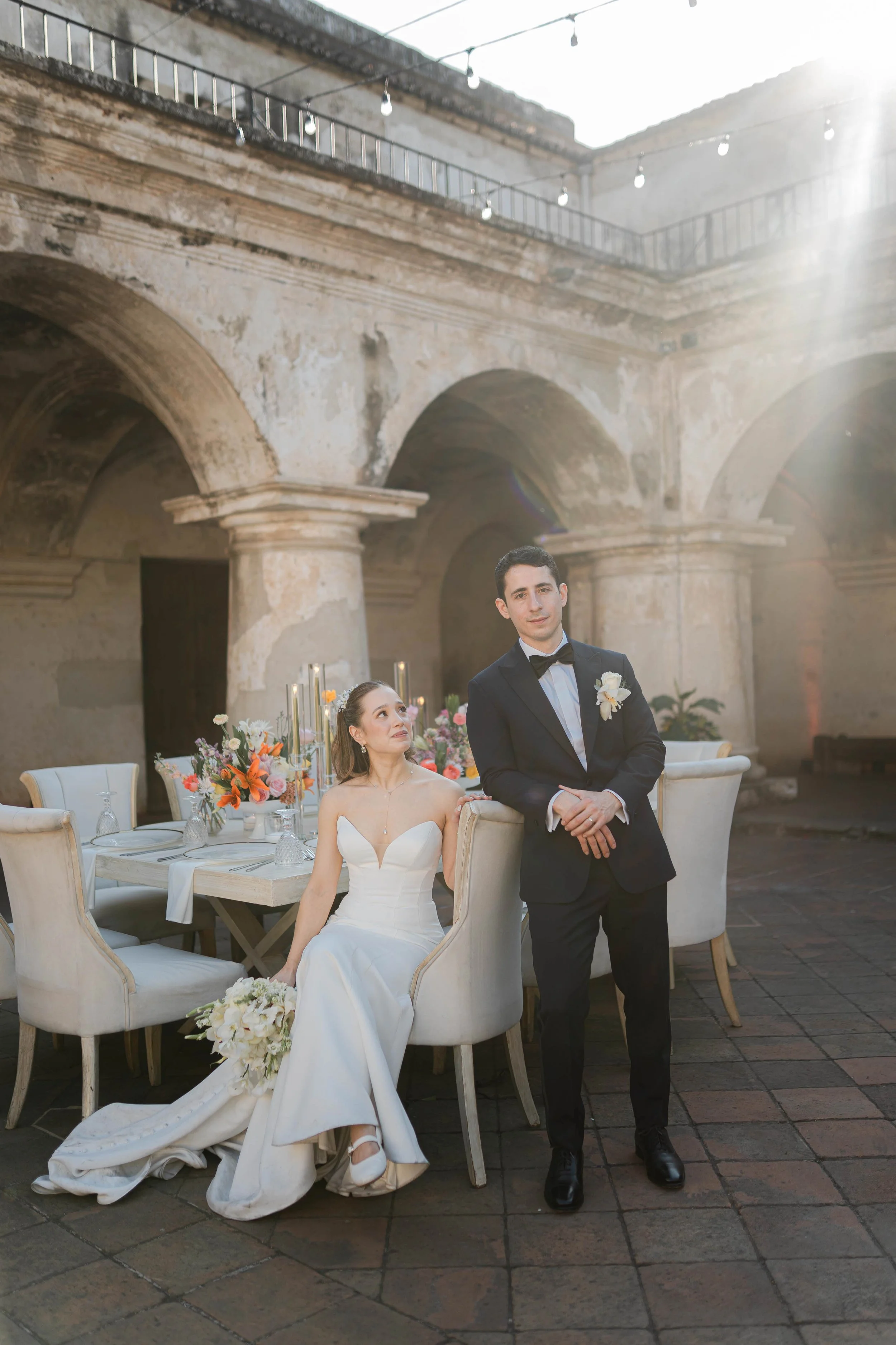Pareja de novios en una boda en un patio antiguo con luz natural y decoraciones florales.