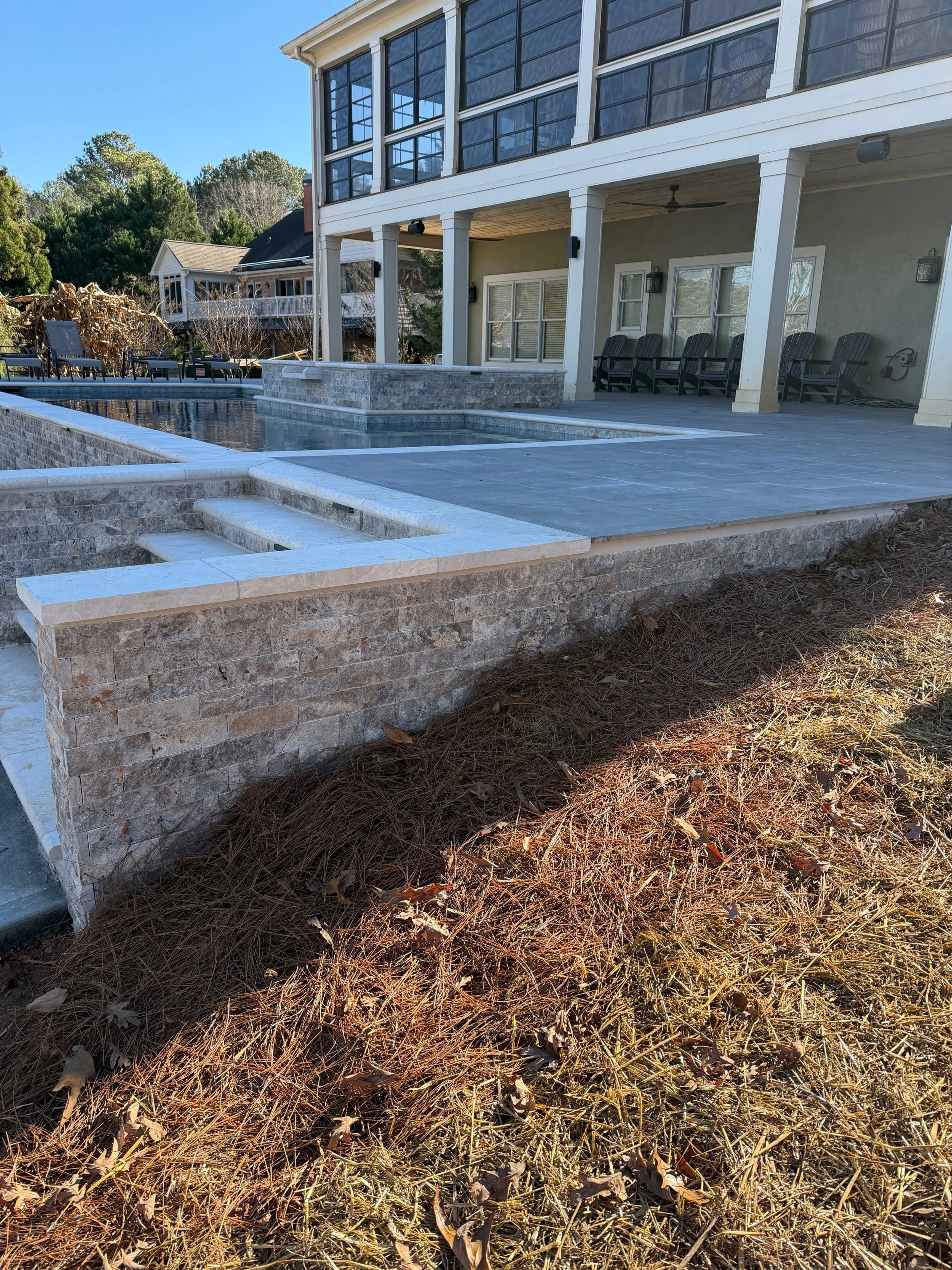 Backyard with a modern house featuring a pool, patio, and outdoor seating area, surrounded by trees and landscaping.