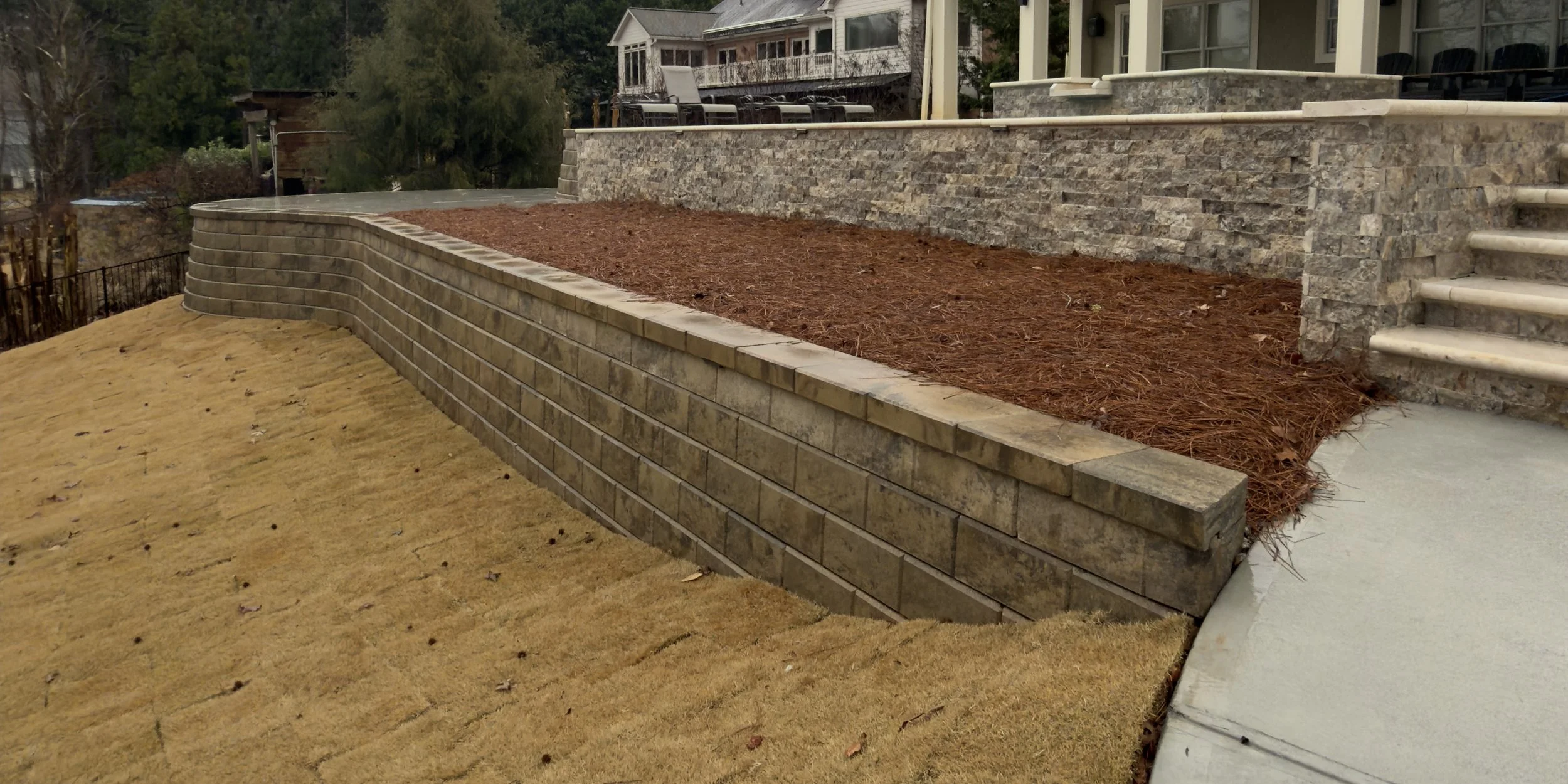 Newly constructed garden retaining wall with brick and stone, with mulched garden bed and stairs leading to elevated house yard.