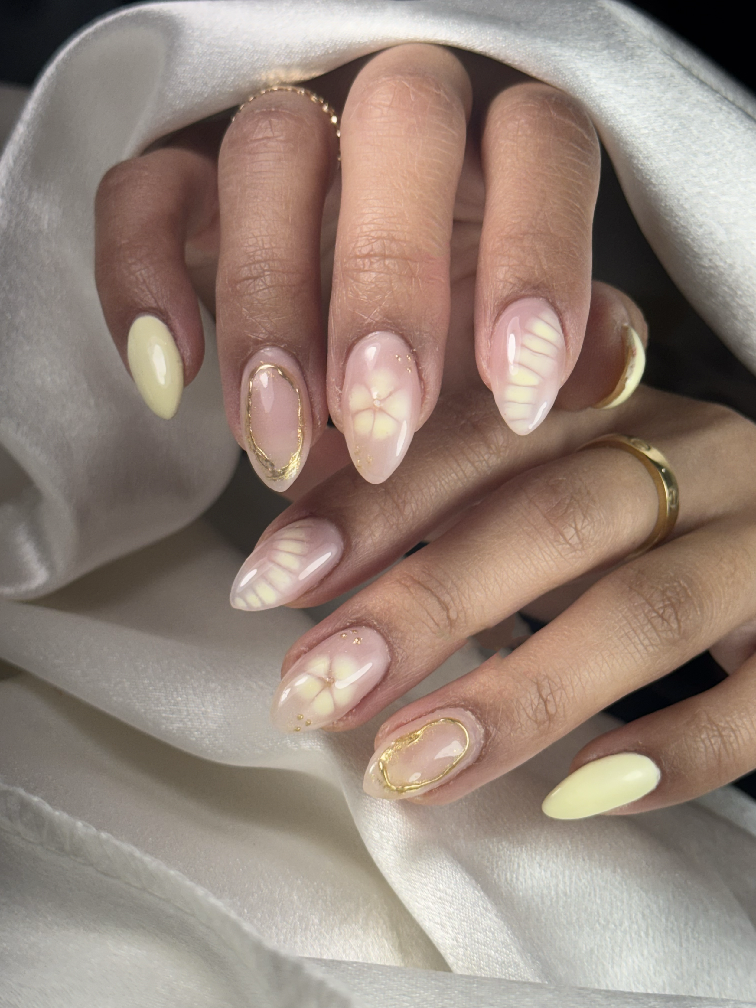 Close-up of hands with manicured nails featuring yellow, white, and gold-accented designs and gold jewelry.